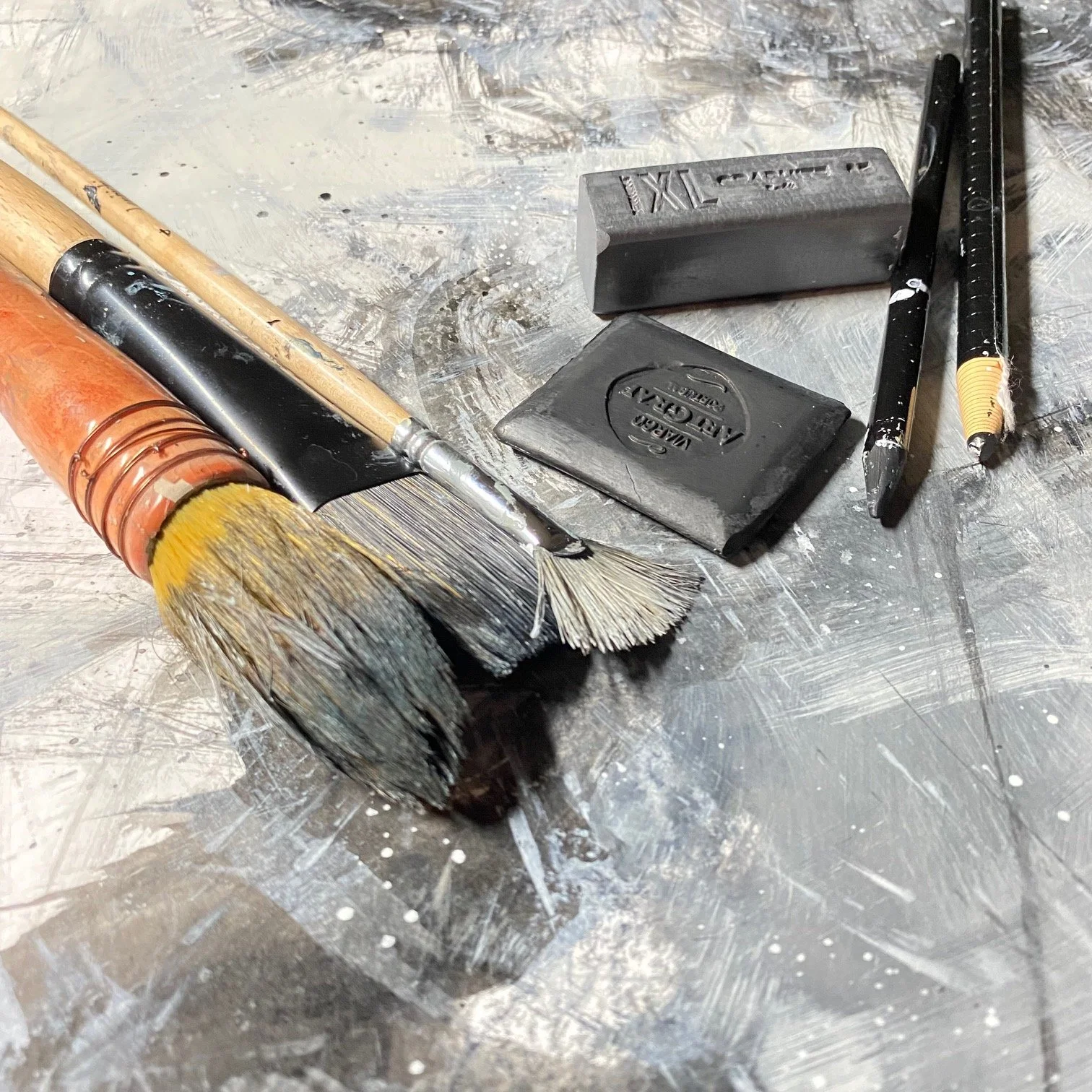 Paintbrushes, erasers, and a black pen on a metallic surface.