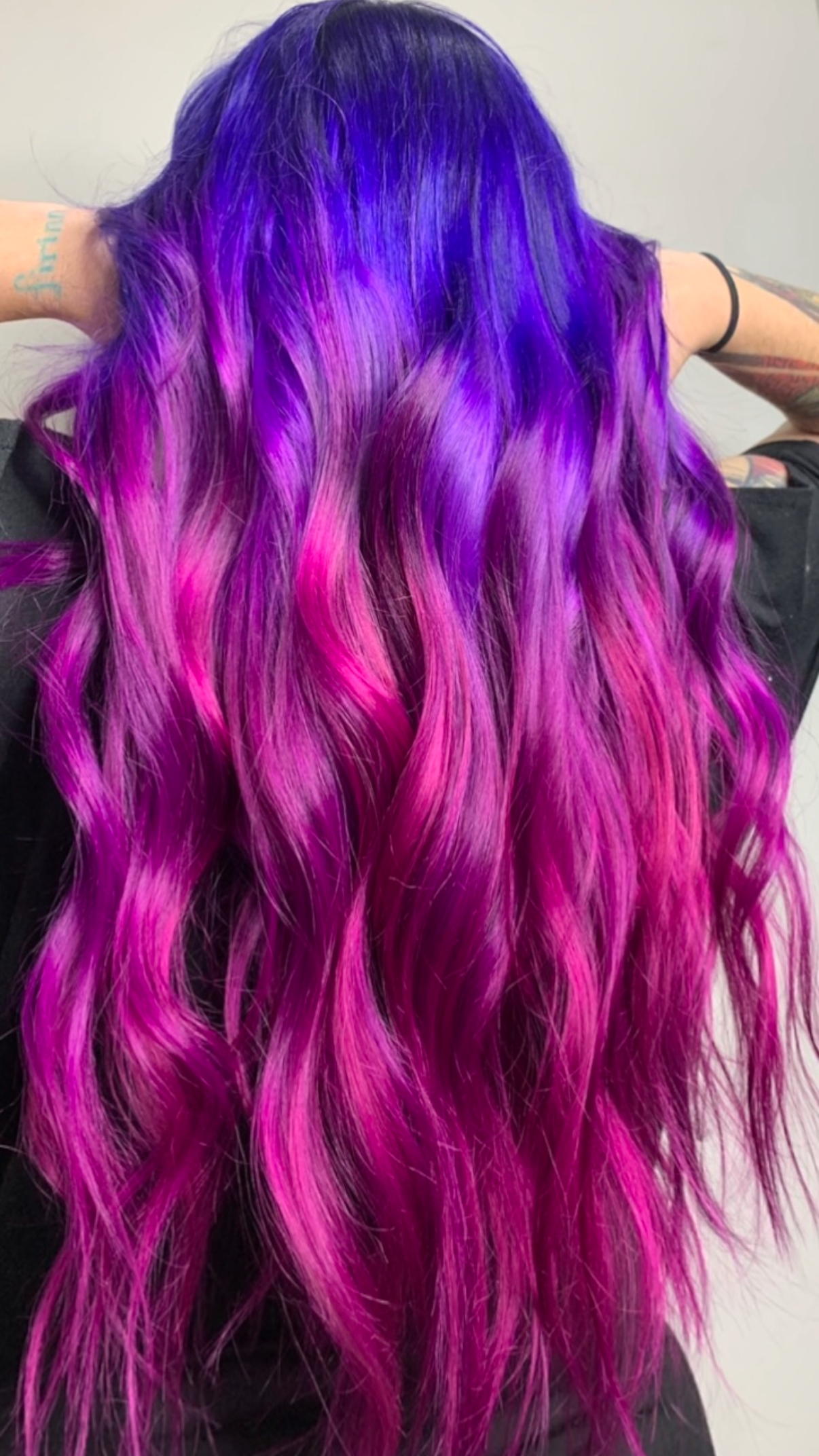 Back view of a person with long, wavy hair dyed in shades of purple, pink, and blue.
