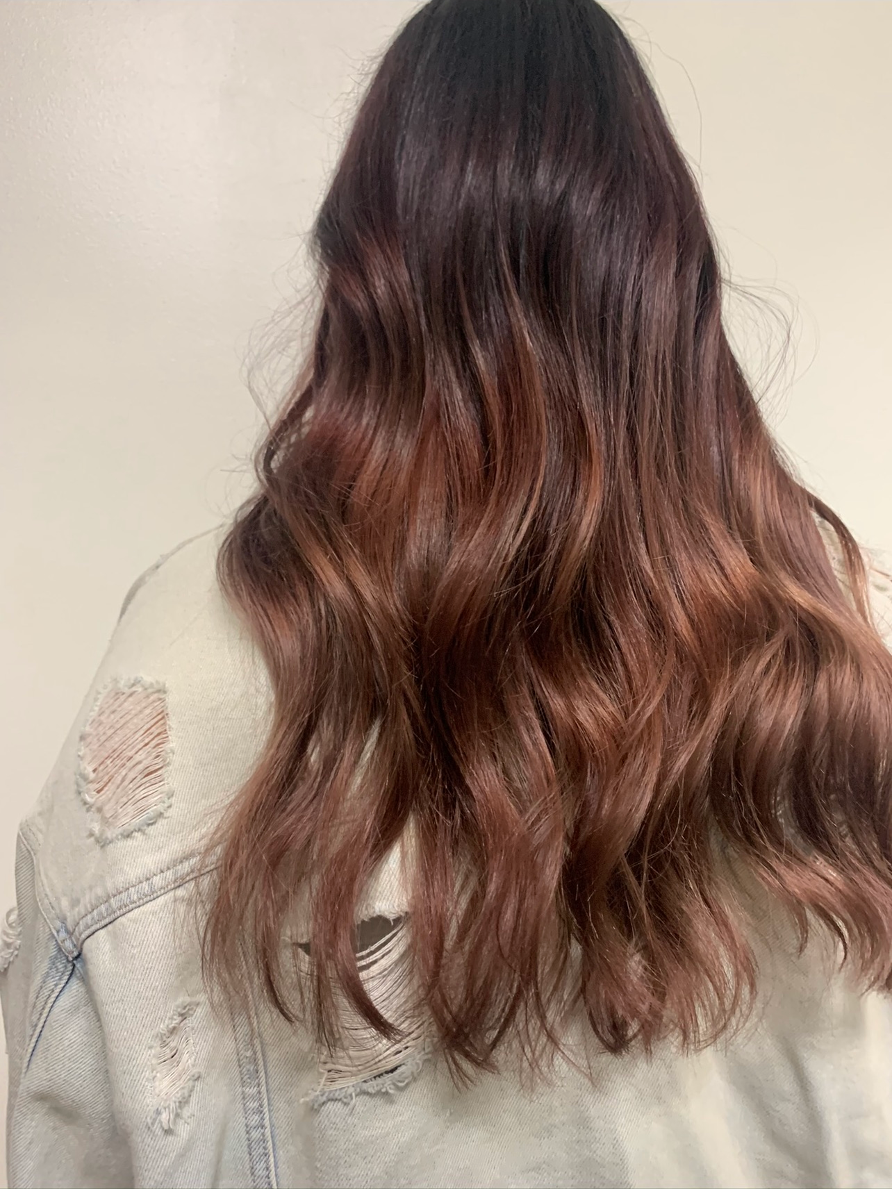 Woman with long, wavy, brown hair wearing a ripped beige denim jacket.