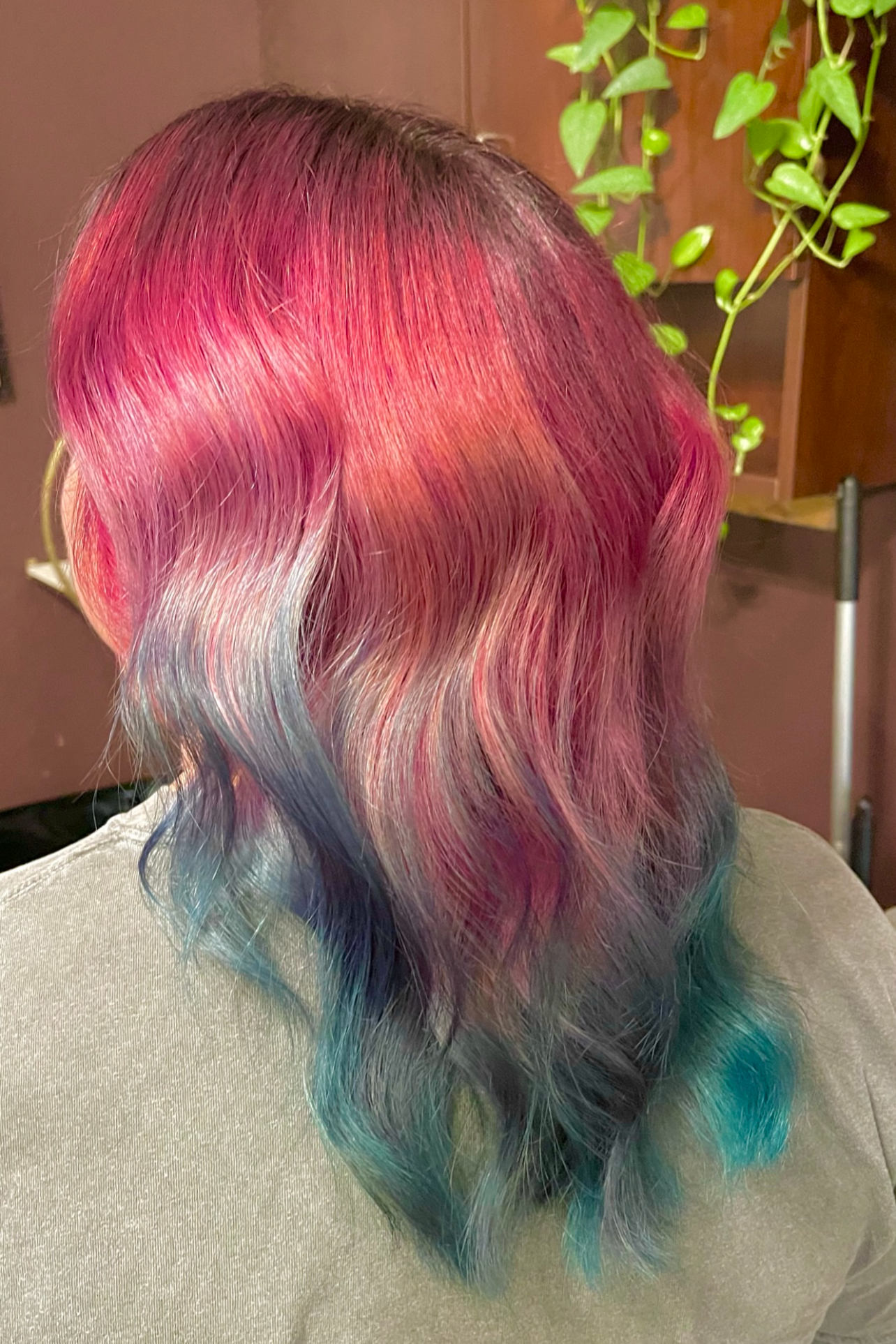 Back of a person with shoulder-length wavy hair dyed in a rainbow gradient, including shades of pink, purple, blue, and green.