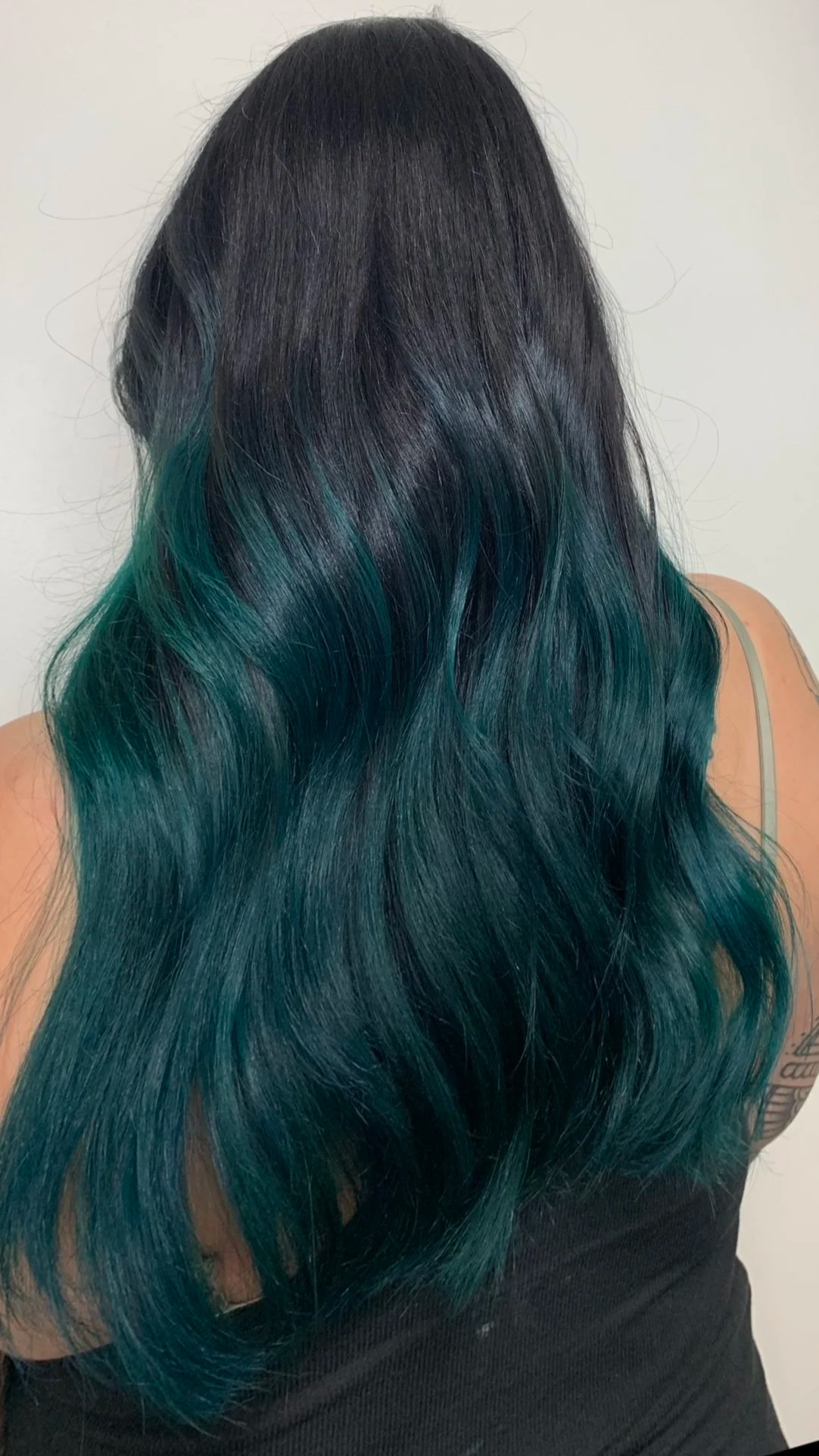 Woman with long, wavy black hair with teal-green ombre highlights.