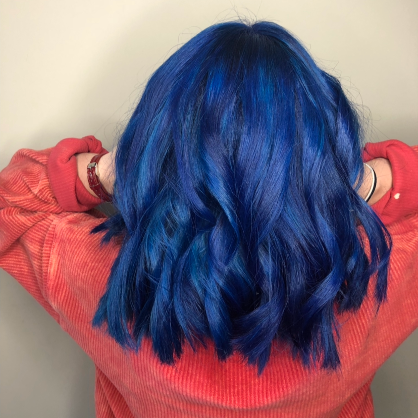 Person with vibrant blue, wavy hair wearing a red hoodie, facing away from the camera.