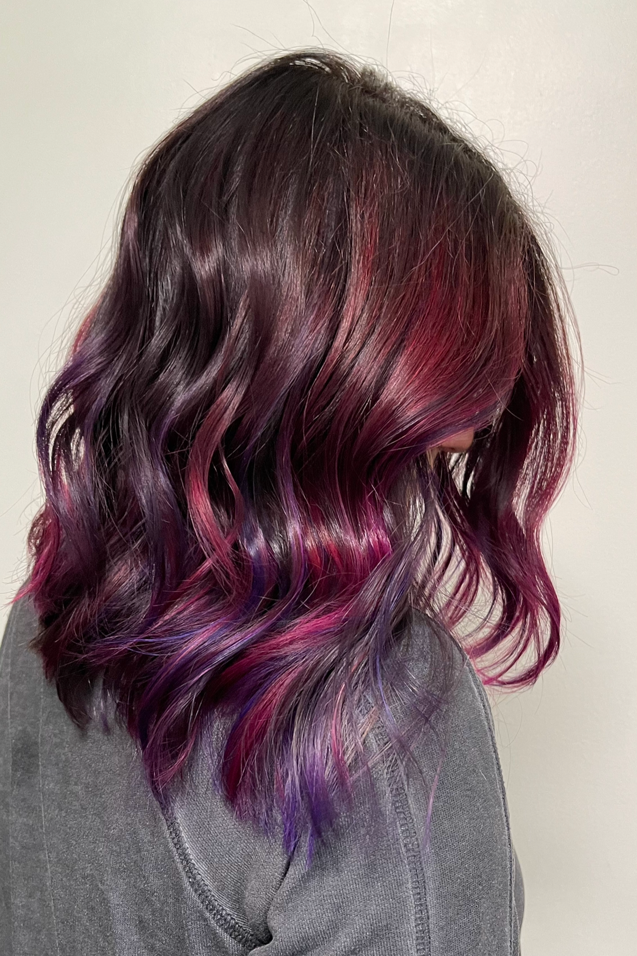 Close-up of a woman's wavy hair dyed with shades of purple, pink, and red.