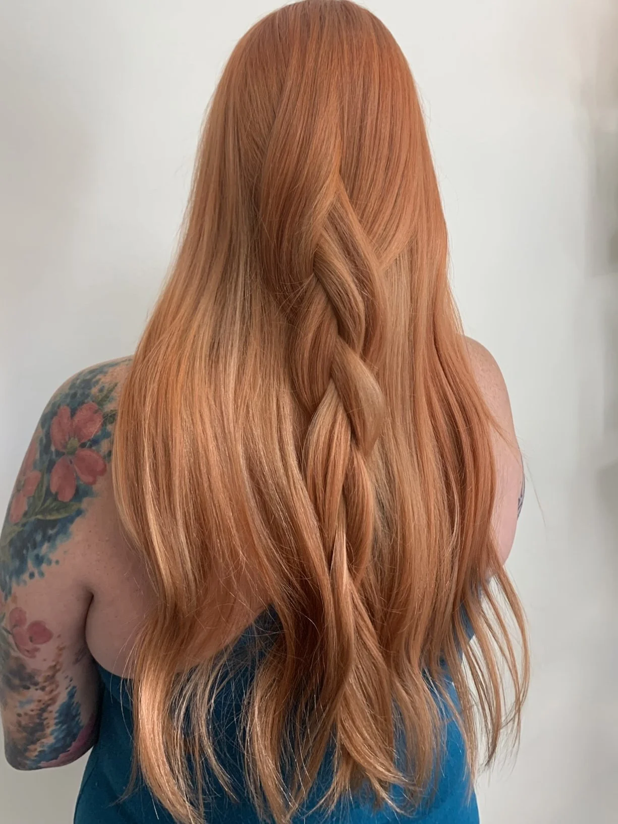 Back view of a woman with long, wavy red hair and a tattoo on her shoulder wearing a dark blue top.