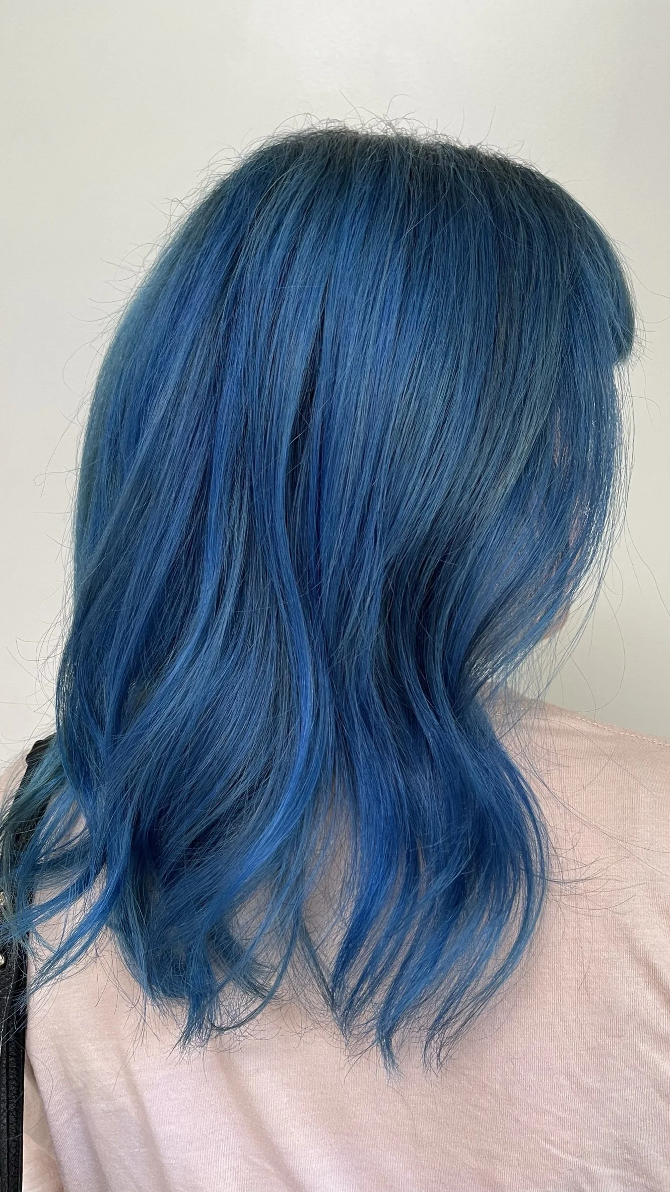 Woman with shoulder-length hair dyed bright blue, with darker roots, wearing a light pink top.