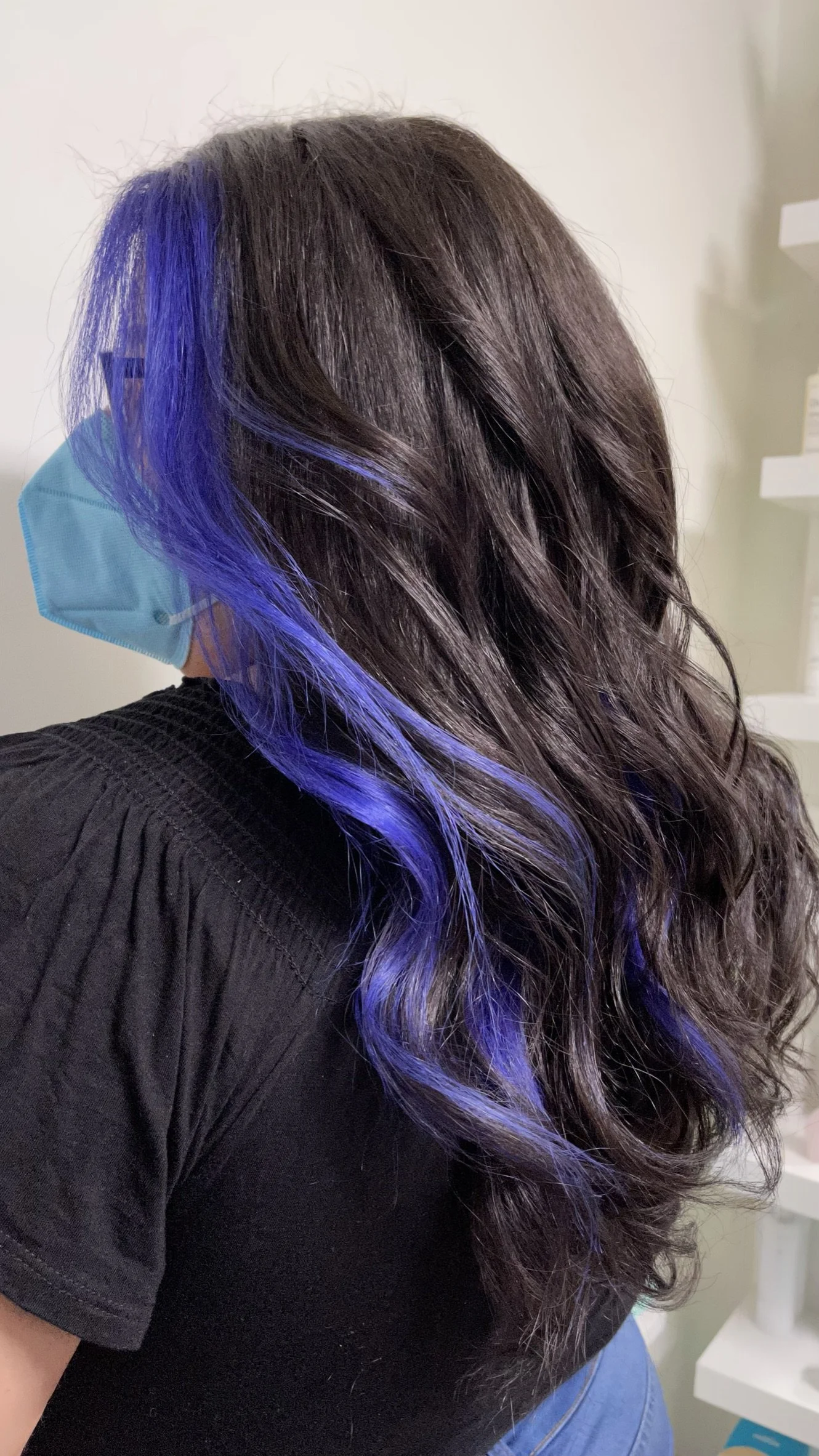 Woman with long wavy brown hair with blue highlights, wearing glasses and a face mask.