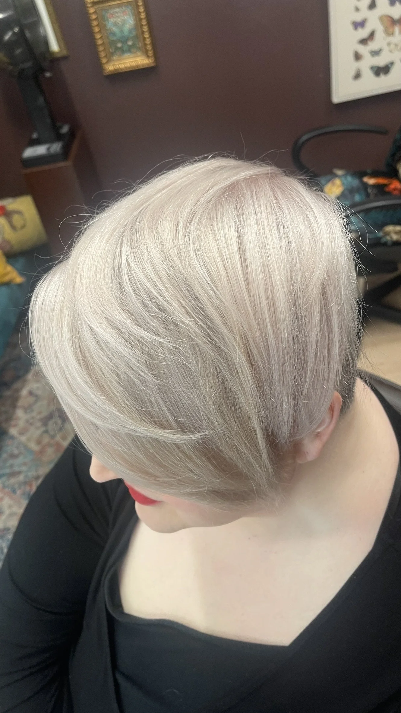 Top view of a woman with short, platinum blonde hair wearing a black top, sitting indoors.