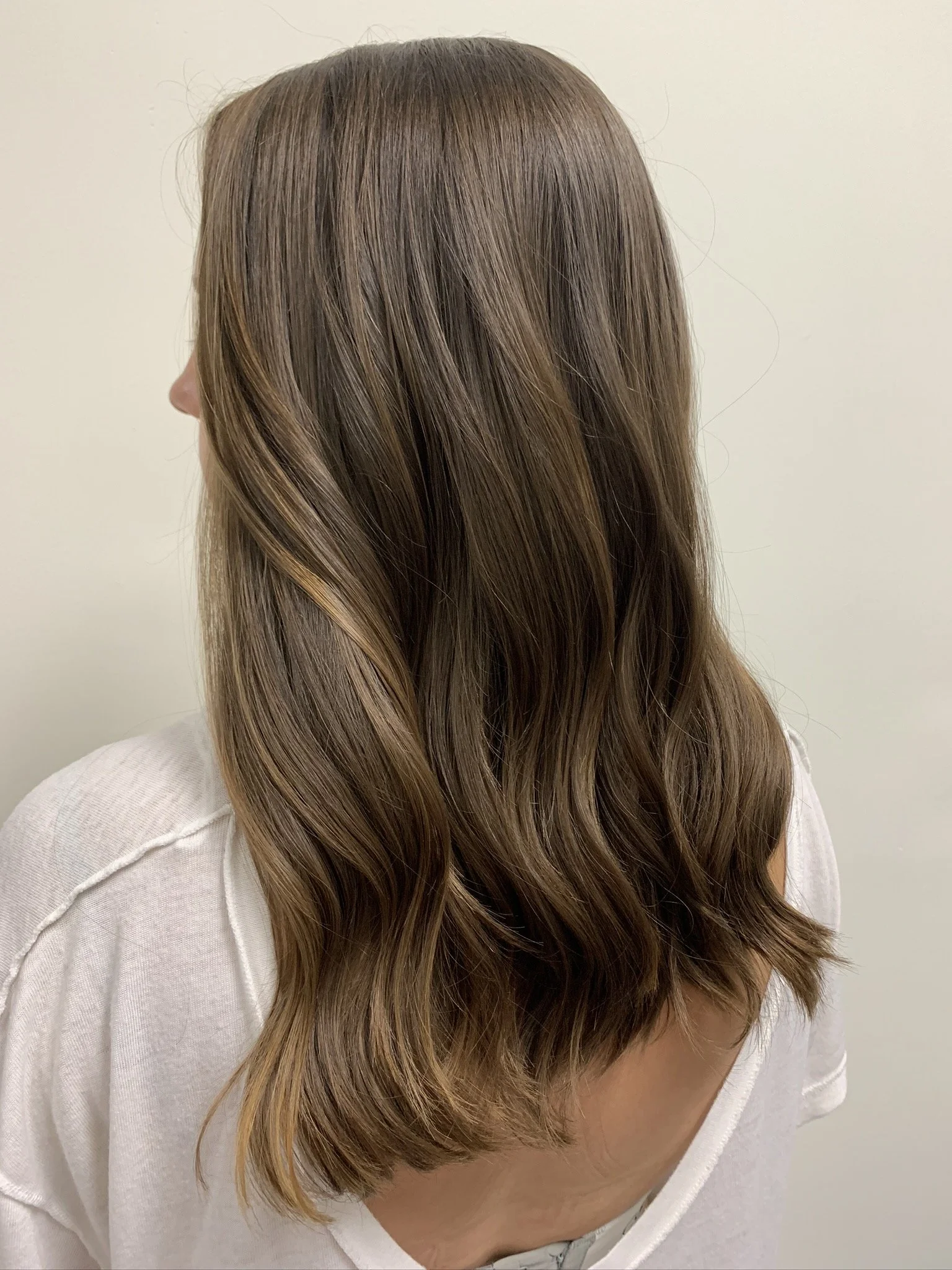 Side view of a woman with shoulder-length brown hair with subtle blonde highlights, wearing a light-colored top.