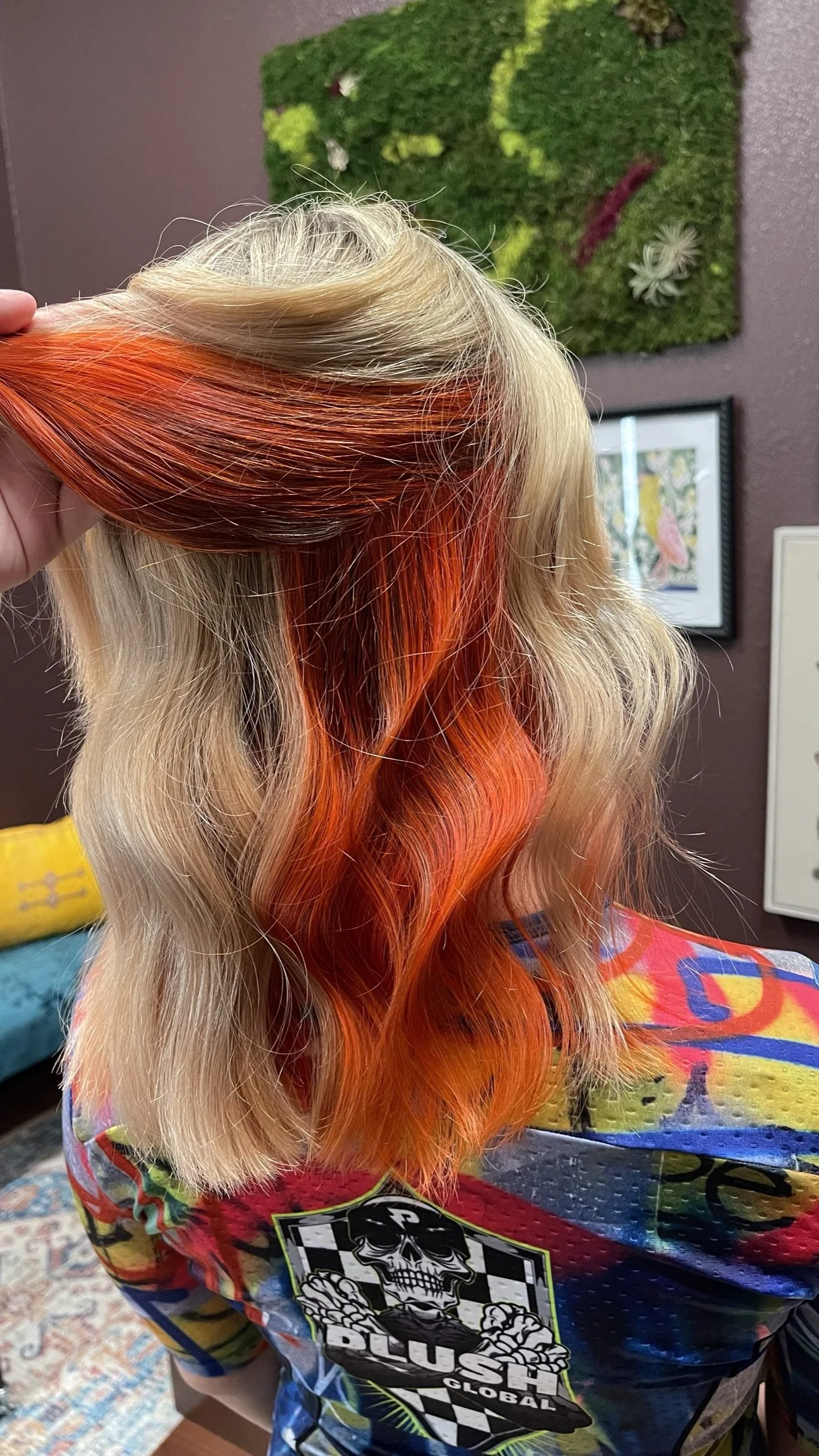 Close-up of a person's hair with blonde and vibrant orange-red coloring, styled with loose waves, held up by their hand.