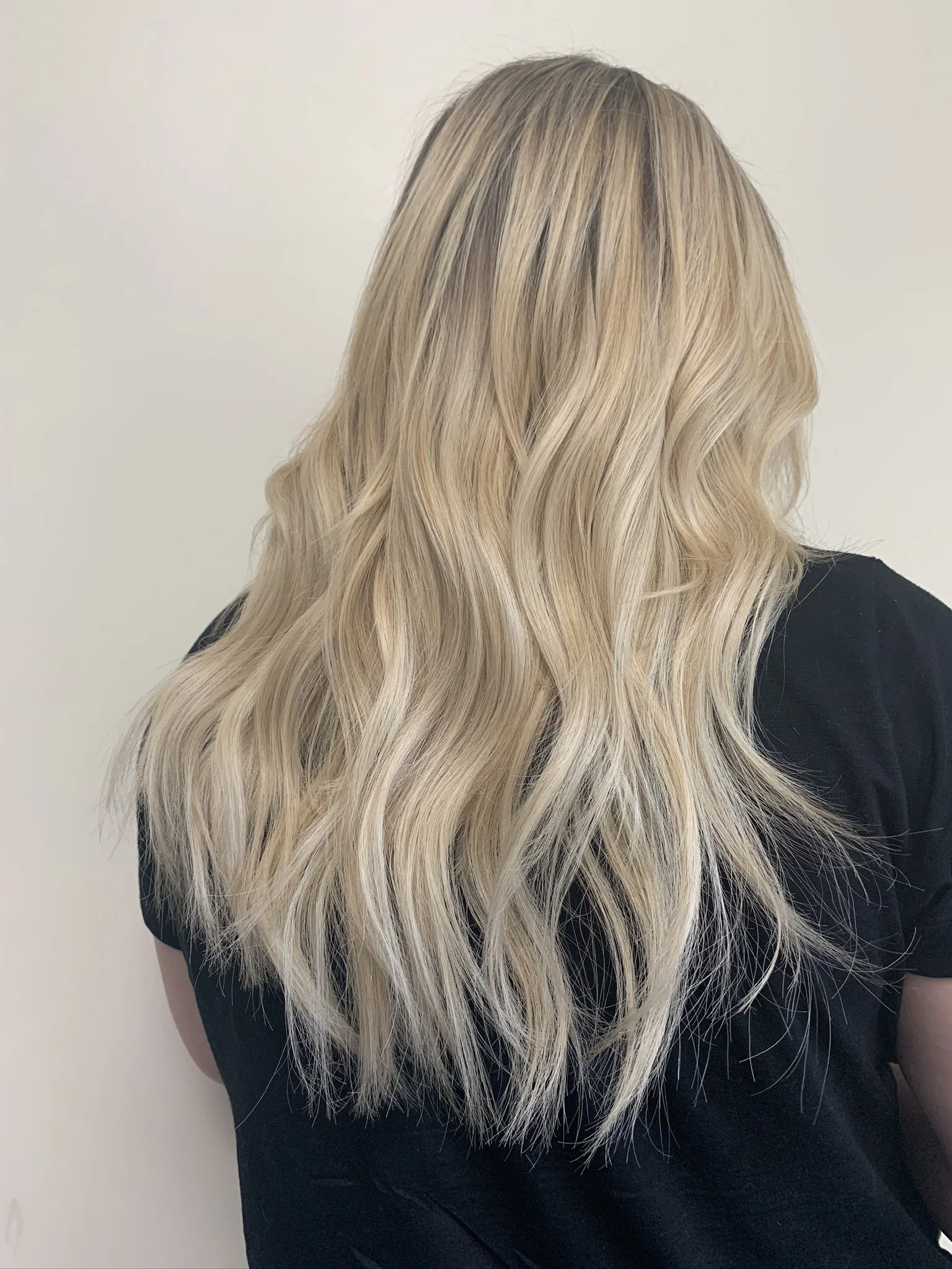 Back view of a woman with long wavy blonde hair wearing a black shirt.