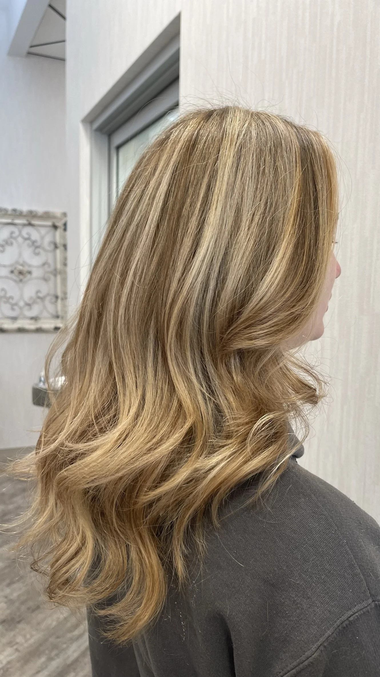 A woman with long, wavy, blonde hair, seen from the side indoors.