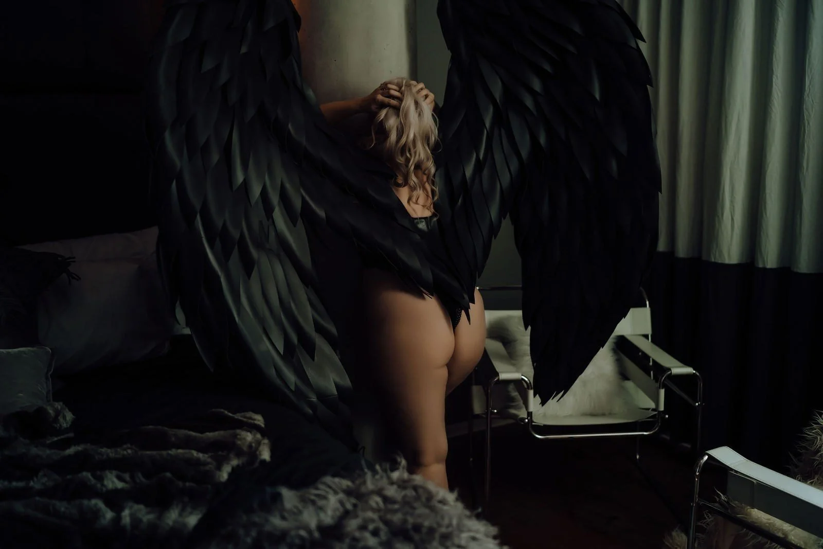 Dark feathered wings spread around a woman in a moody studio, Angel Wings boudoir photos, Nashville