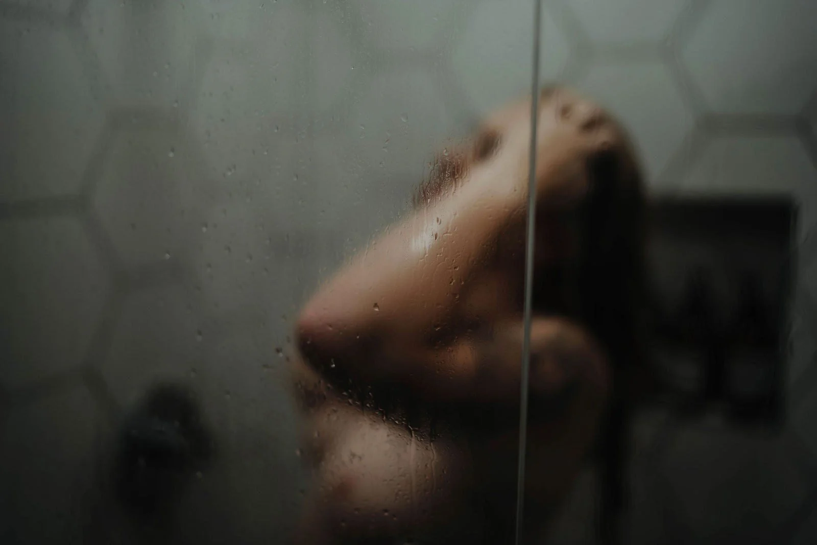 Woman with arm raised in a steamy shower behind frosted glass, Nashville boudoir add-on sets