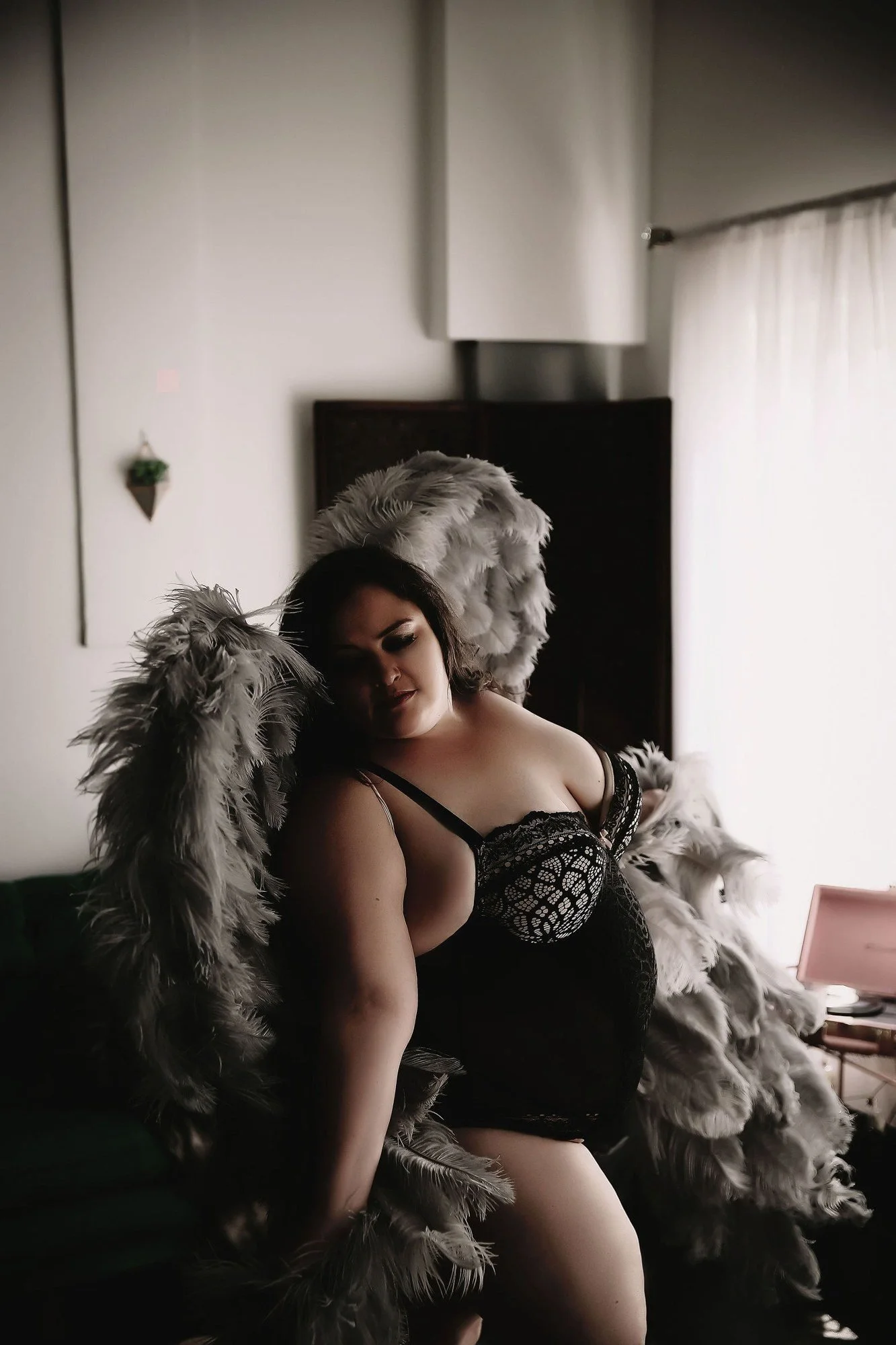 Woman in lace lingerie wearing fluffy grey angel wings by a window, Nashville boudoir add-on sets