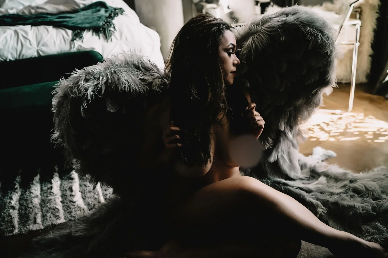 Woman framed by white feathered wings in dramatic shadows, Nashville boudoir add-on sets