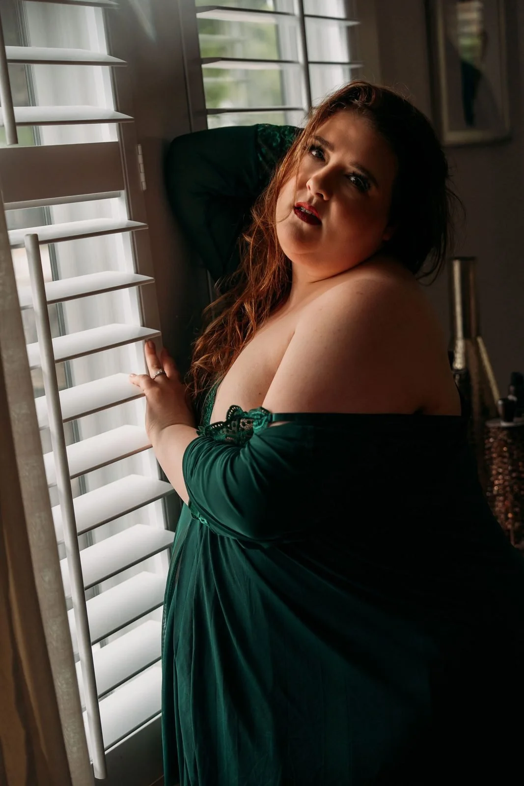 Client in a green robe posing by the window shutters