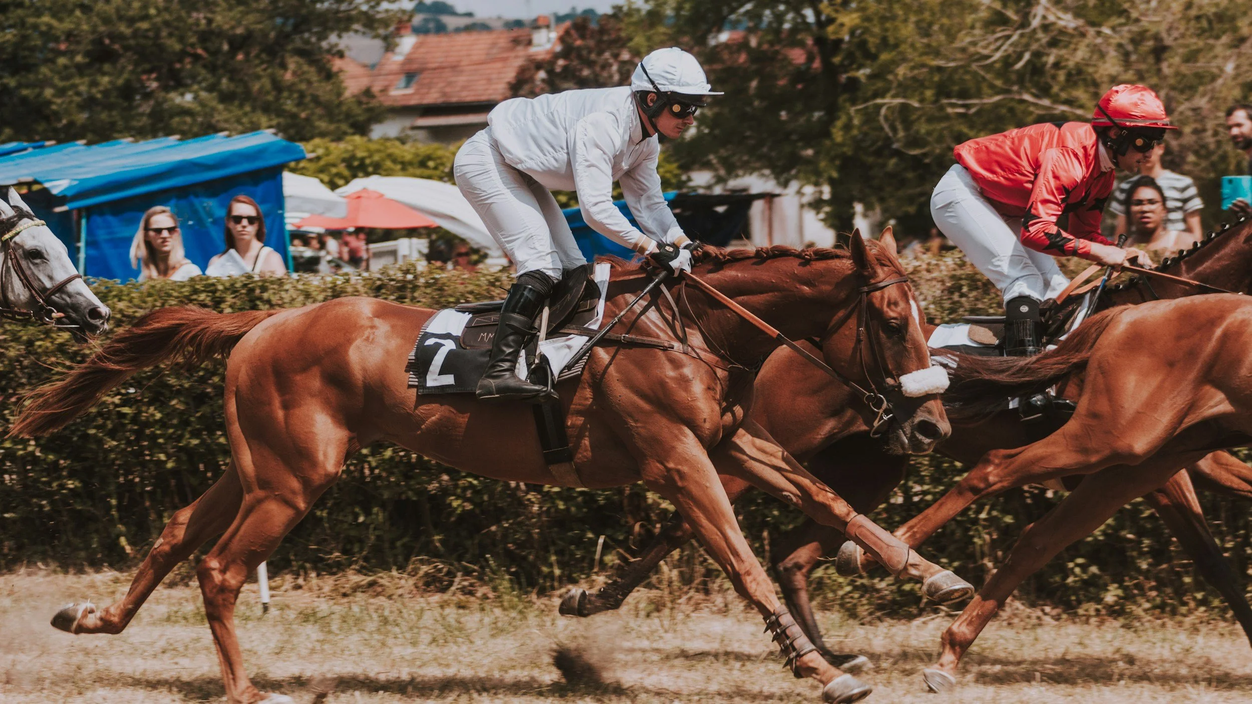 Two jockeys riding racehorses during a horse race, with spectators watching in the background.