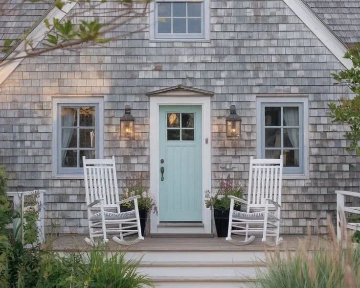 a photo of a charming cozy clapboard weather beach house exterior with two white rocking chairs on the front porch.