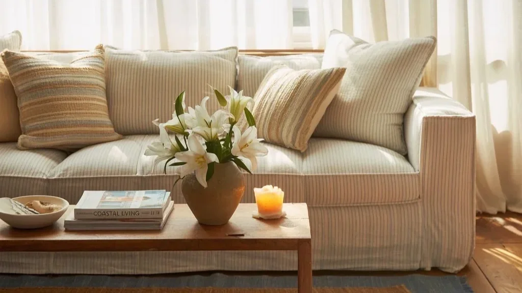 a coastal living room with a beige sofa and fresh cut flowers on a wooden coffee table.