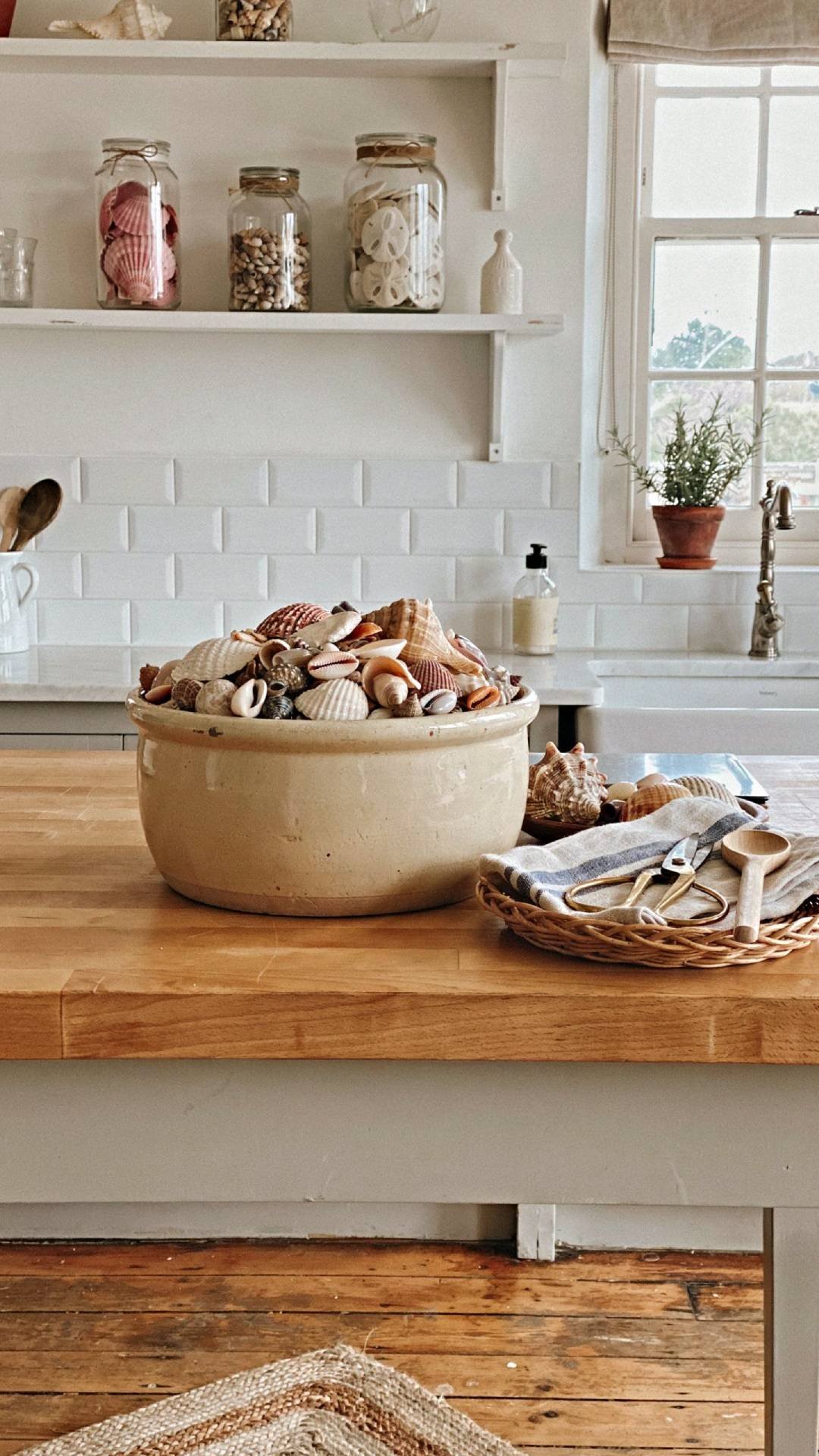 Full kitchen shot with a vintage dough bowl filled with shells as a centerpiece on an island, glass jars of shells on open shelving, natural light, warm coastal cottage atmosphere, photorealistic