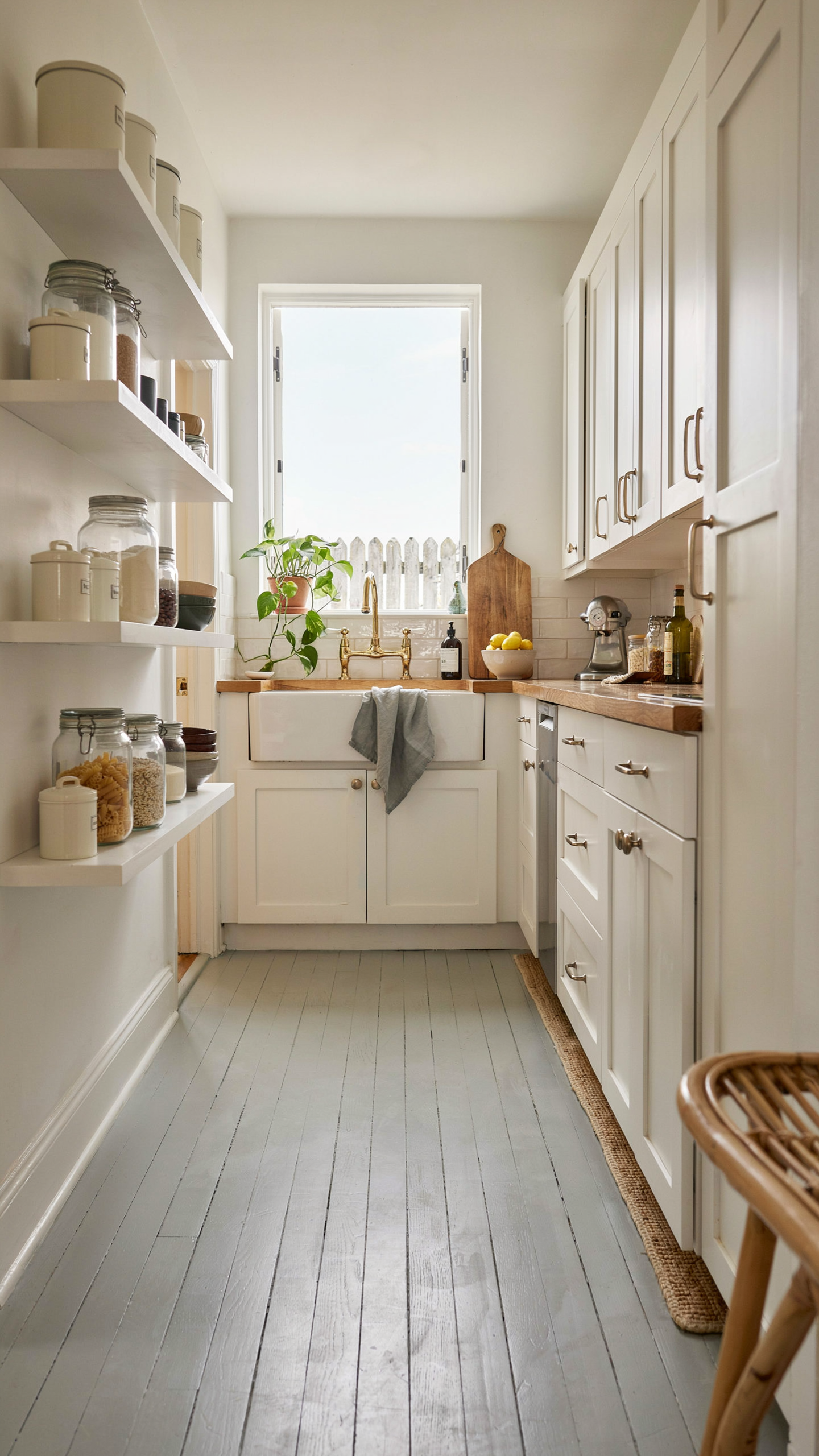 a coastal kitchen with open shelving lined with cream enamelware canisters and clear glass jars, white cabinetry, warm wood counters, natural window light