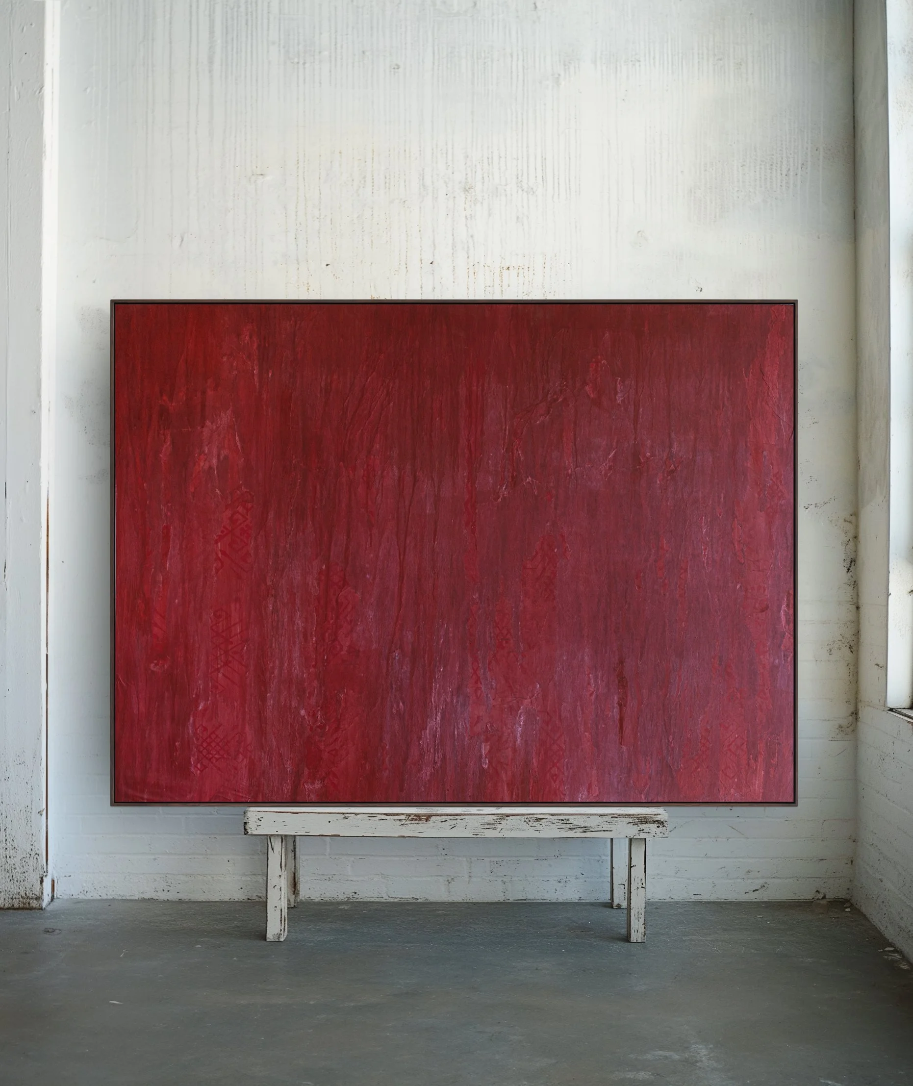 A large rectangular red painting on a white wooden stand in a room with white walls and concrete floor.