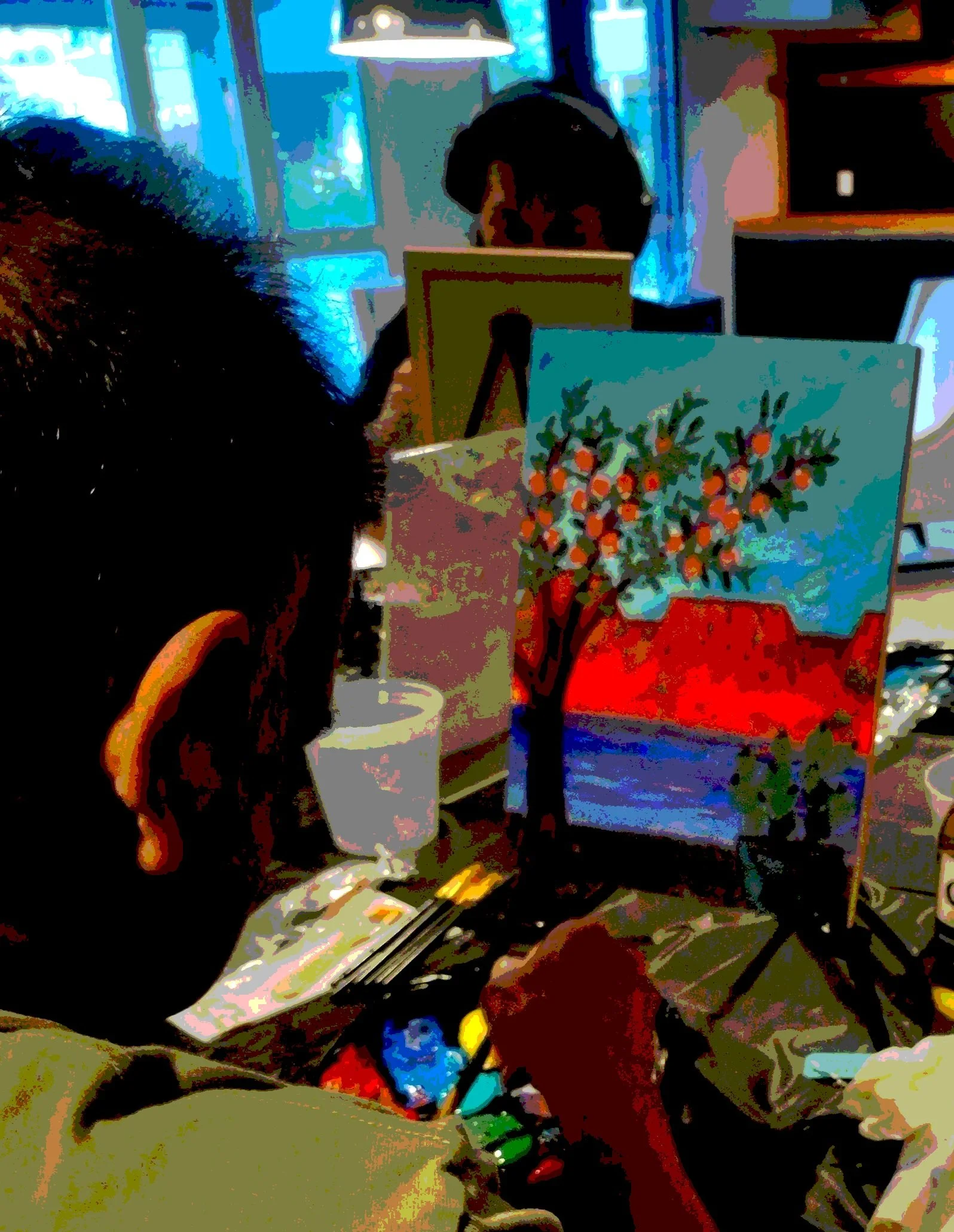 A group of diverse people inside a modern building with large windows showing city buildings outside. Some individuals are holding up colorful paintings of landscapes and nature scenes. The group is smiling and appears to be at an art or community event.