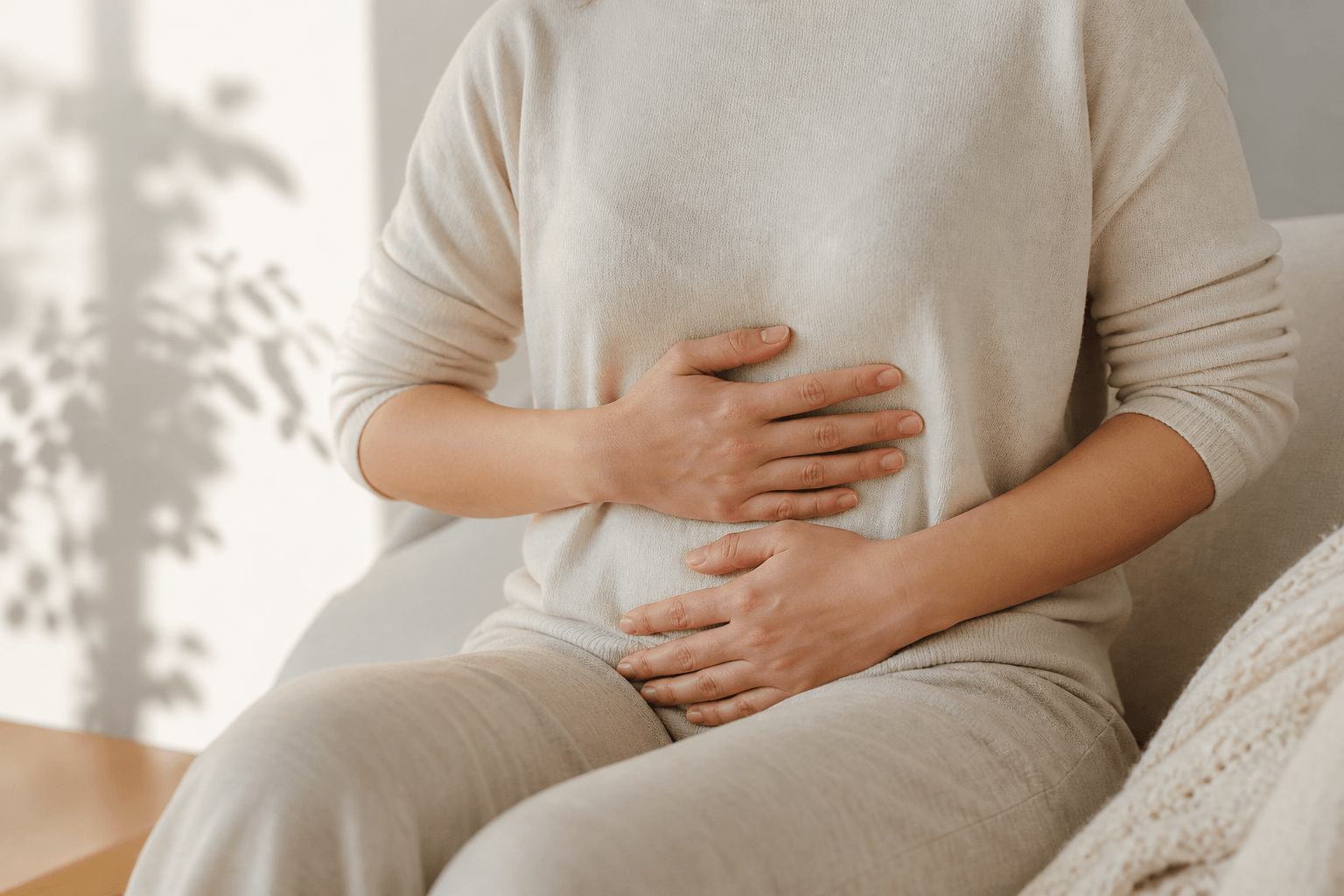 Person resting hands on abdomen in soft natural light representing gut involvement in long COVID and ME/CFS