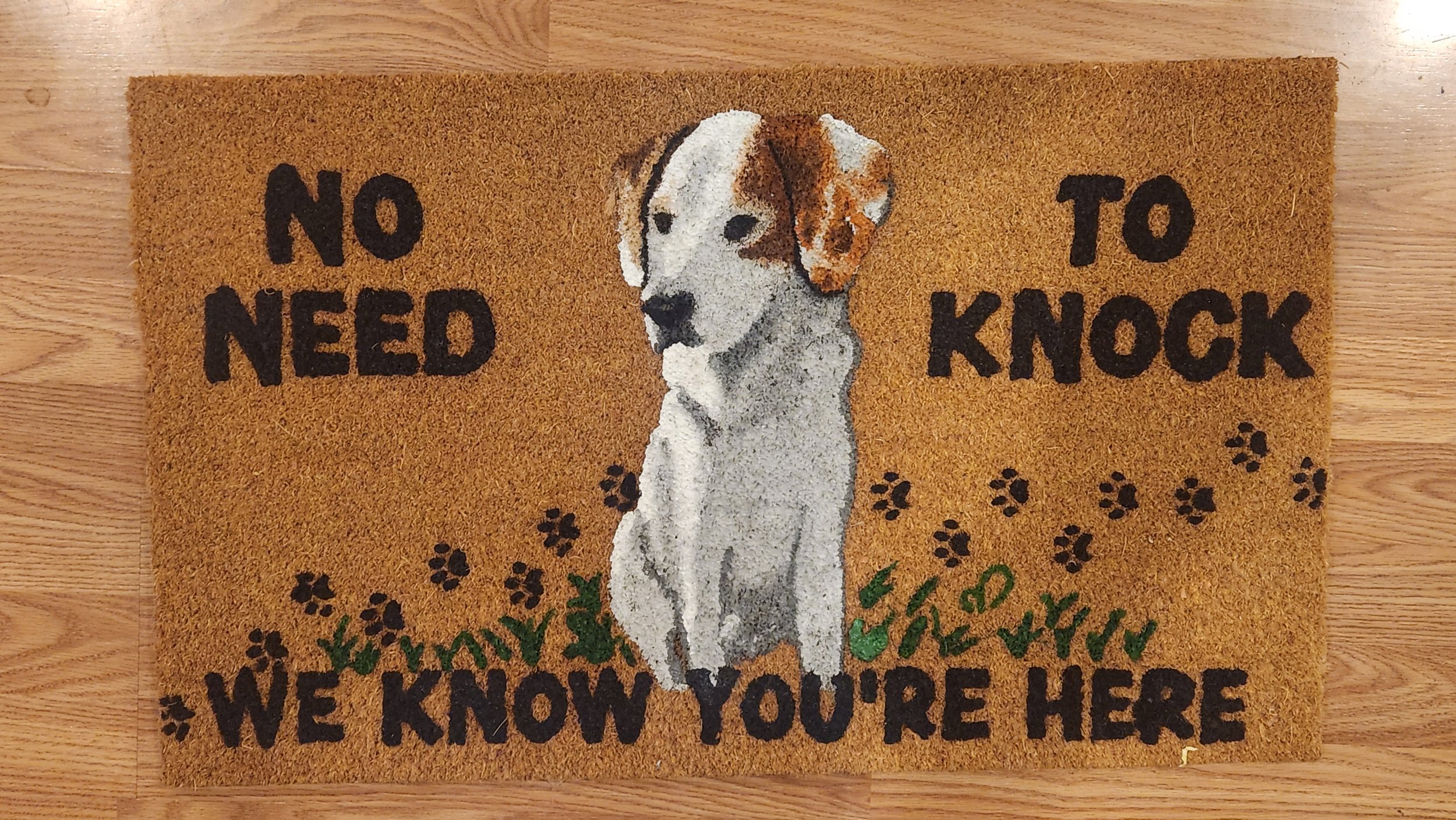 Doormat with a picture of a dog, paw prints, and the text 'No need to knock, we know you're here.'