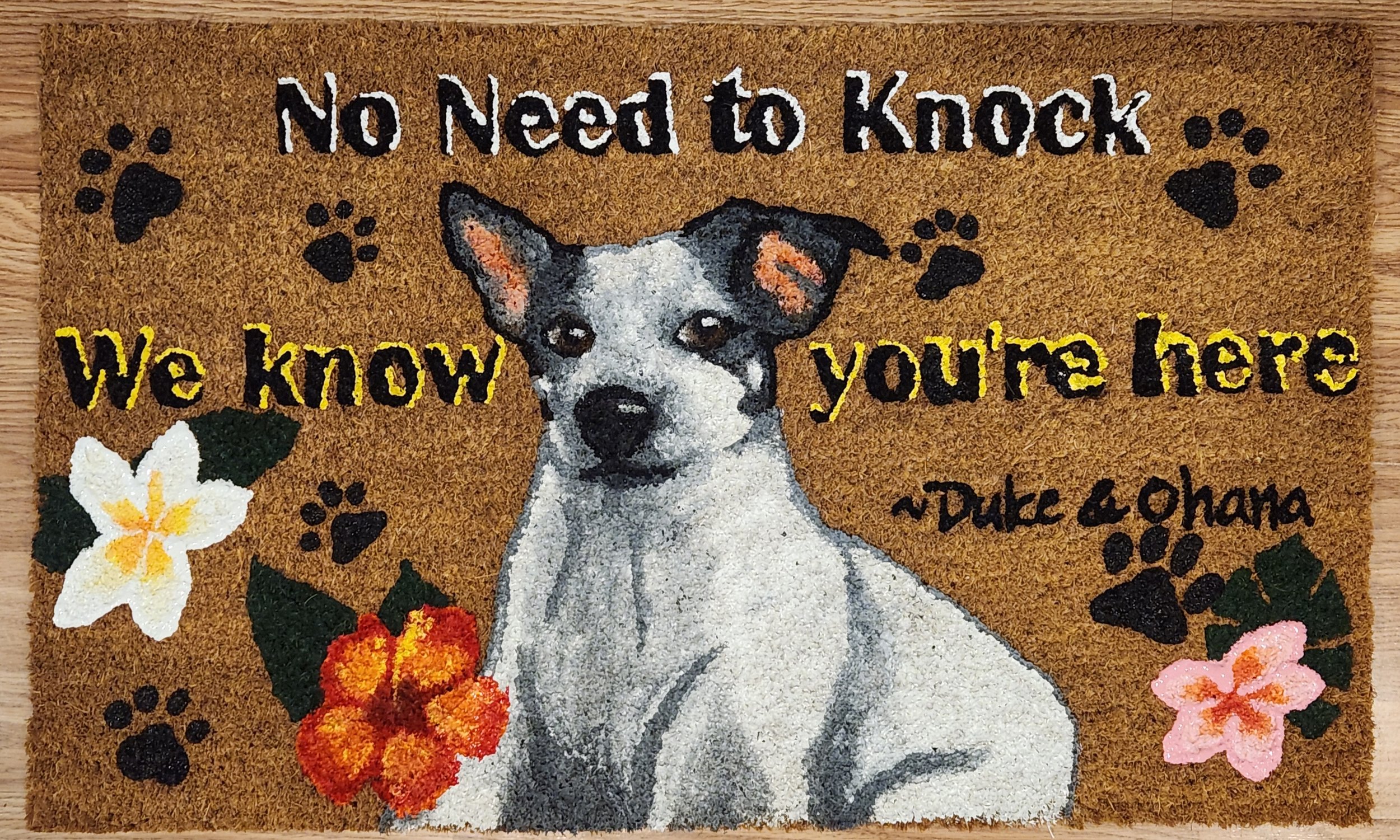 Doormat with a dog illustration, floral decorations, paw prints, and the text 'No need to knock. We know you're here. ~Duke & Chana'.