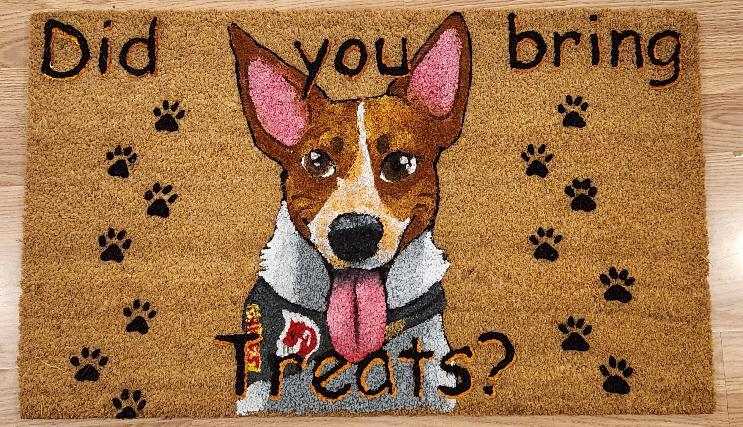 Decorative doormat with a cartoon image of a dog, pink ears, and a pink tongue, surrounded by black paw prints. The mat has the text 'Did you bring treats?' written on it.