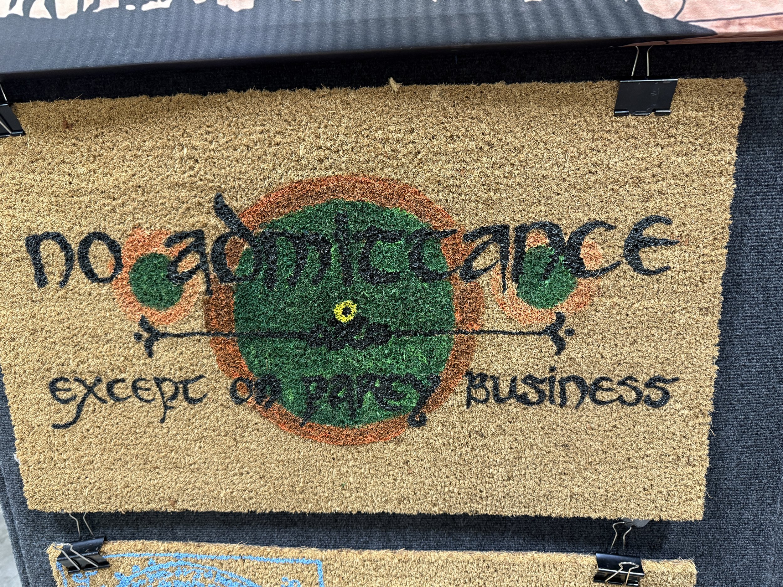 A doormat with the phrase "no experience except on face business" and a cartoonish green face with two green eye patches, a small yellow nose, and a black mustache, framed by a red circle.