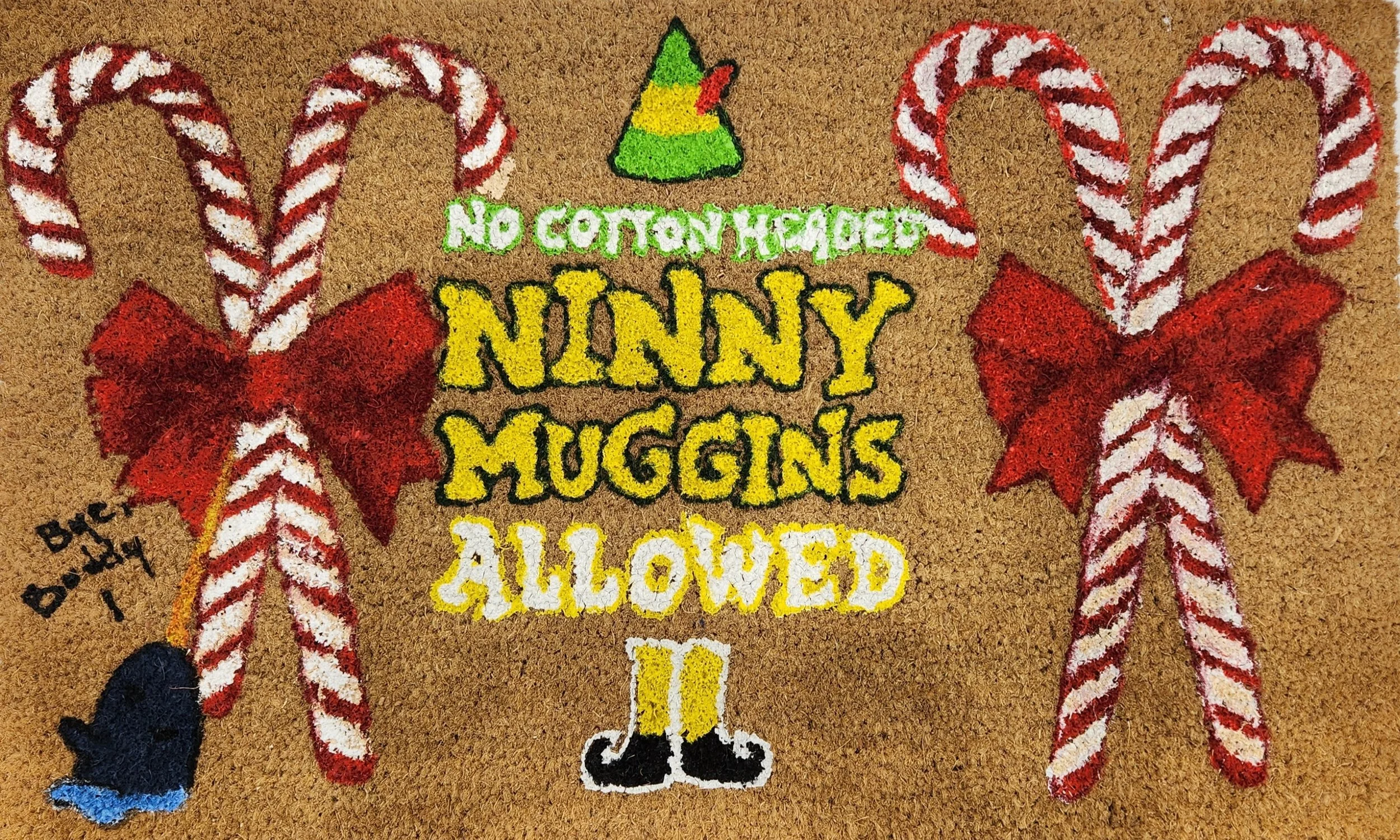 Colorful holiday-shaped door mat with candy canes, a small Santa hat, and playful text saying 'No candy handed, Nanny Muggins allowed'.