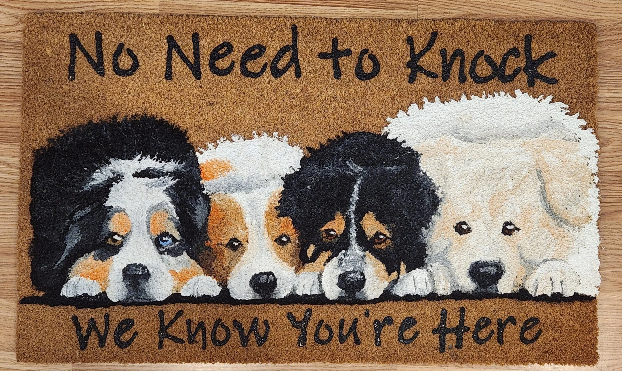 Decorative doormat with the phrase "No Need to Knock, We Know You're Here" and images of four adorable puppy faces in a row.
