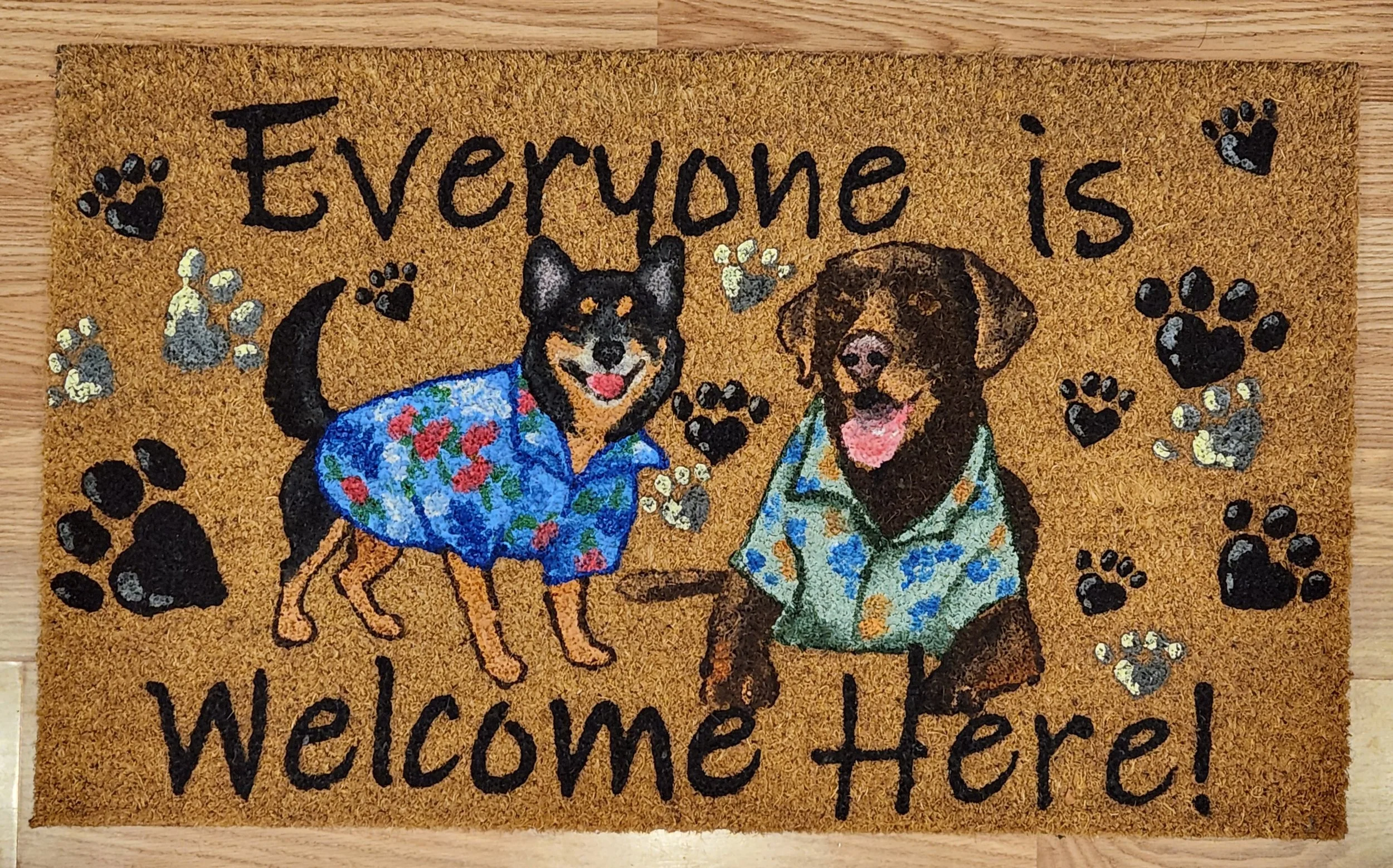 Decorative welcome mat featuring two happy dogs wearing Hawaiian shirts, surrounded by paw prints and the text "Everyone is Welcome Here!"
