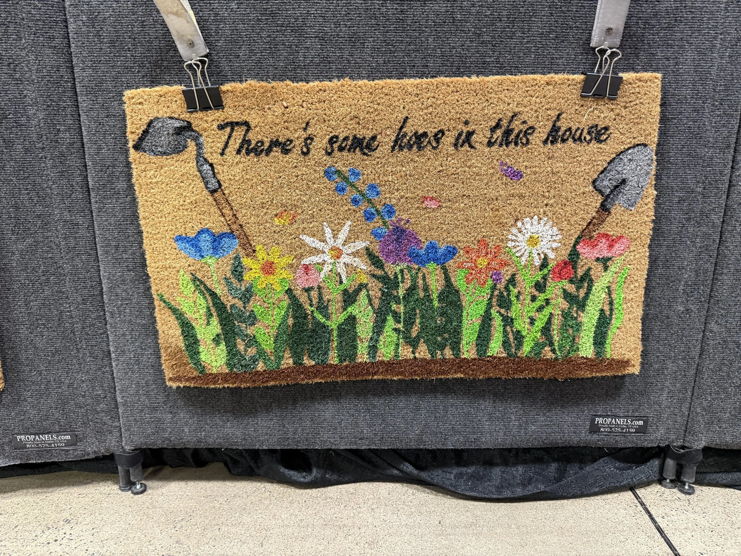 A decorative doormat with colorful flowers and shovels, and the text 'There's some love in this house' written on it.