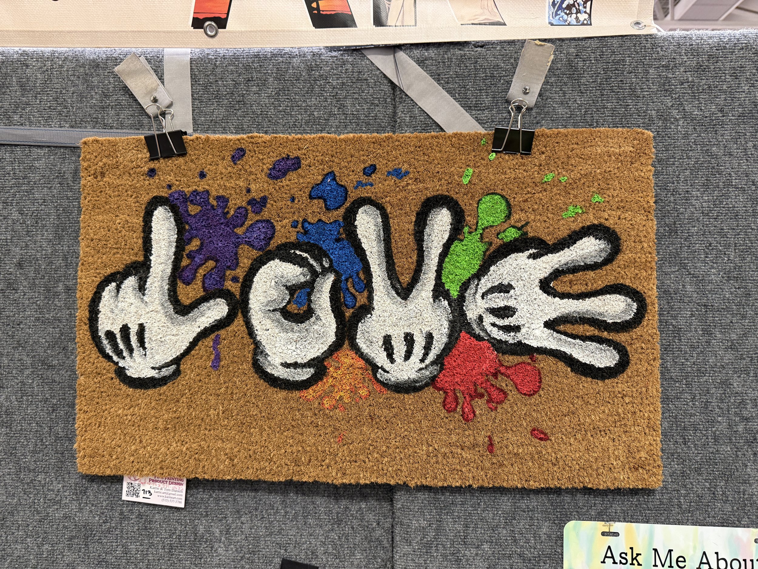 Doormat with the word 'LOVE' spelled out with three gloved hands making different gestures, and colorful paint splashes in the background.