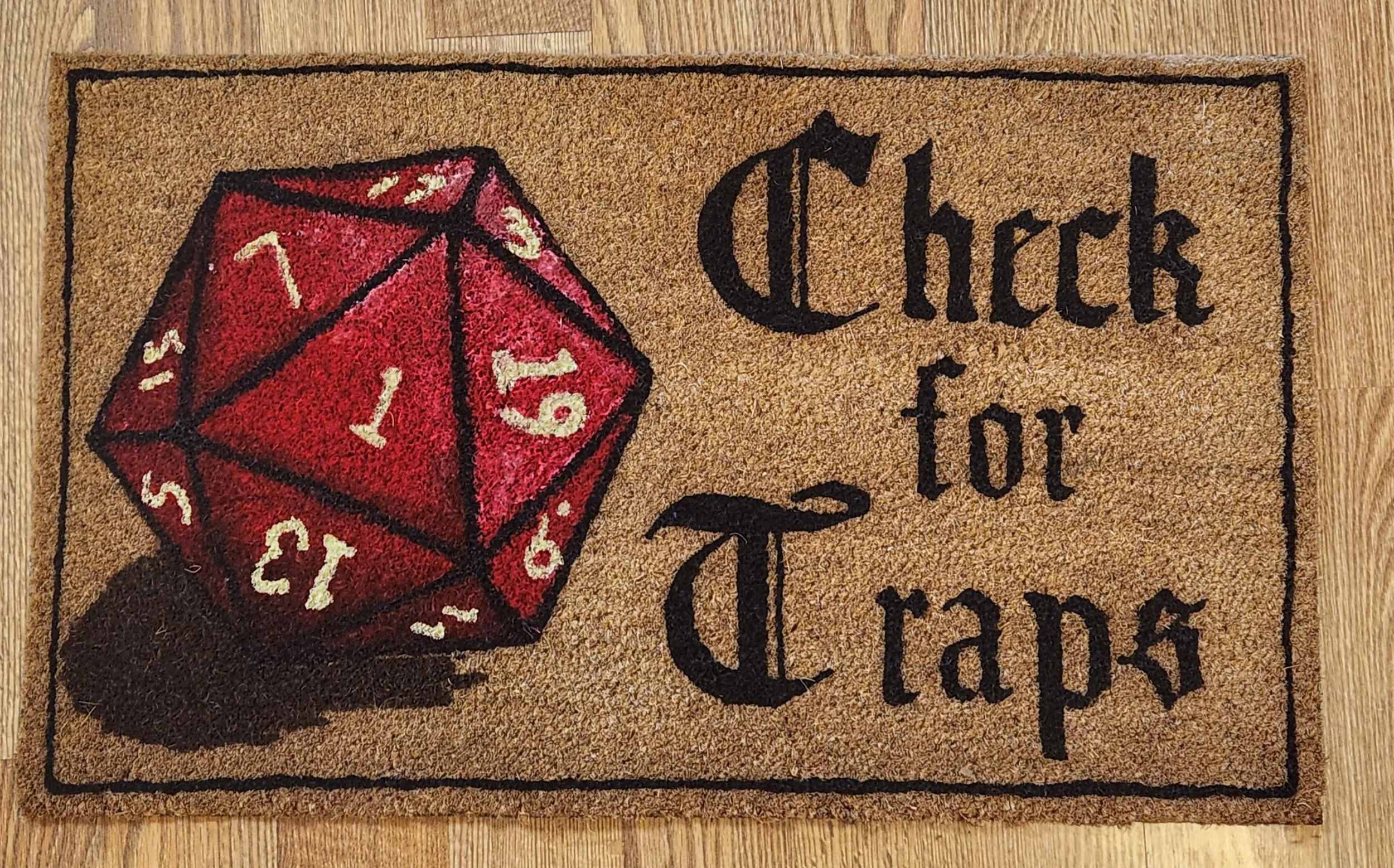 Decorative doormat with a red twenty-sided die and the text 'Check for Trap' in black Gothic-style font.