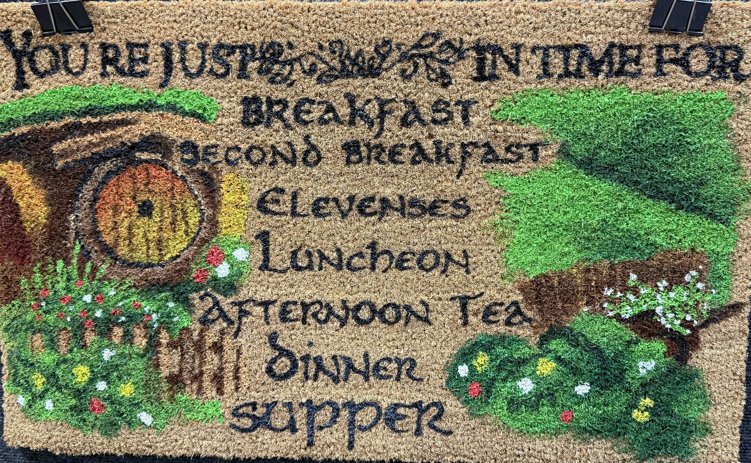 A decorative doormat with a gardening theme and a message about breakfast, lunch, and dinner routines.