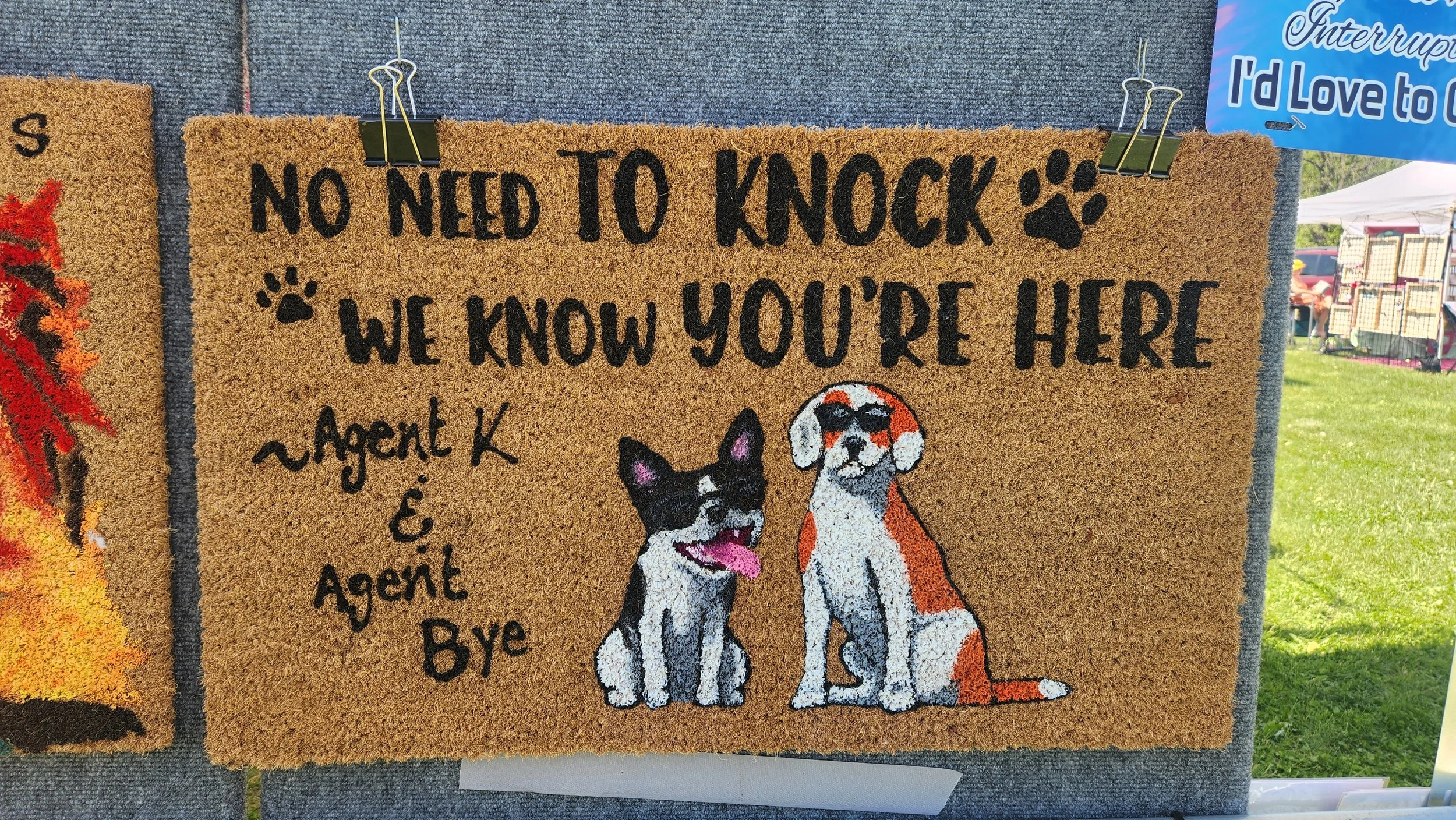 A decorative welcome mat with cartoon images of a happy black and white dog and a brown and white dog, along with the text 'No need to knock, we know you're here - Agent K & Agent B'.