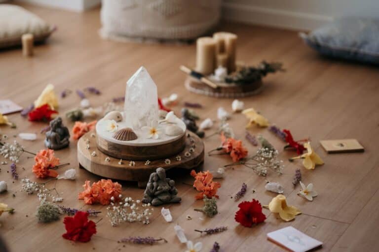 A crystal point surrounded by small candles, shells, flowers, and decorative objects on a wooden floor.