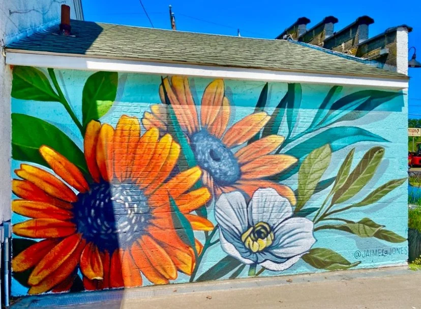 Street mural of orange flowers, a bee, and green leaves painted on a building wall.