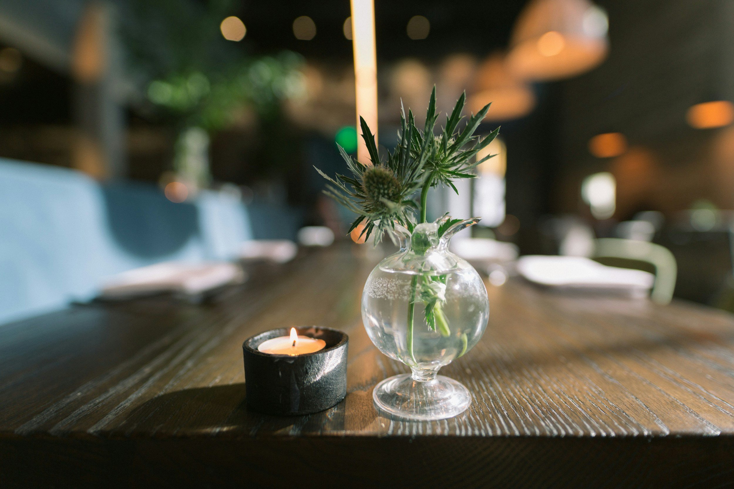 Small candle and glass vase with flowers on wooden table in a restaurant.