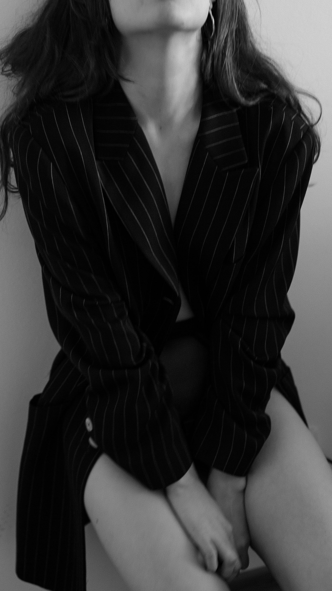 Black and white photo of a woman wearing a black pinstripe blazer, sitting with her arms and legs crossed.
