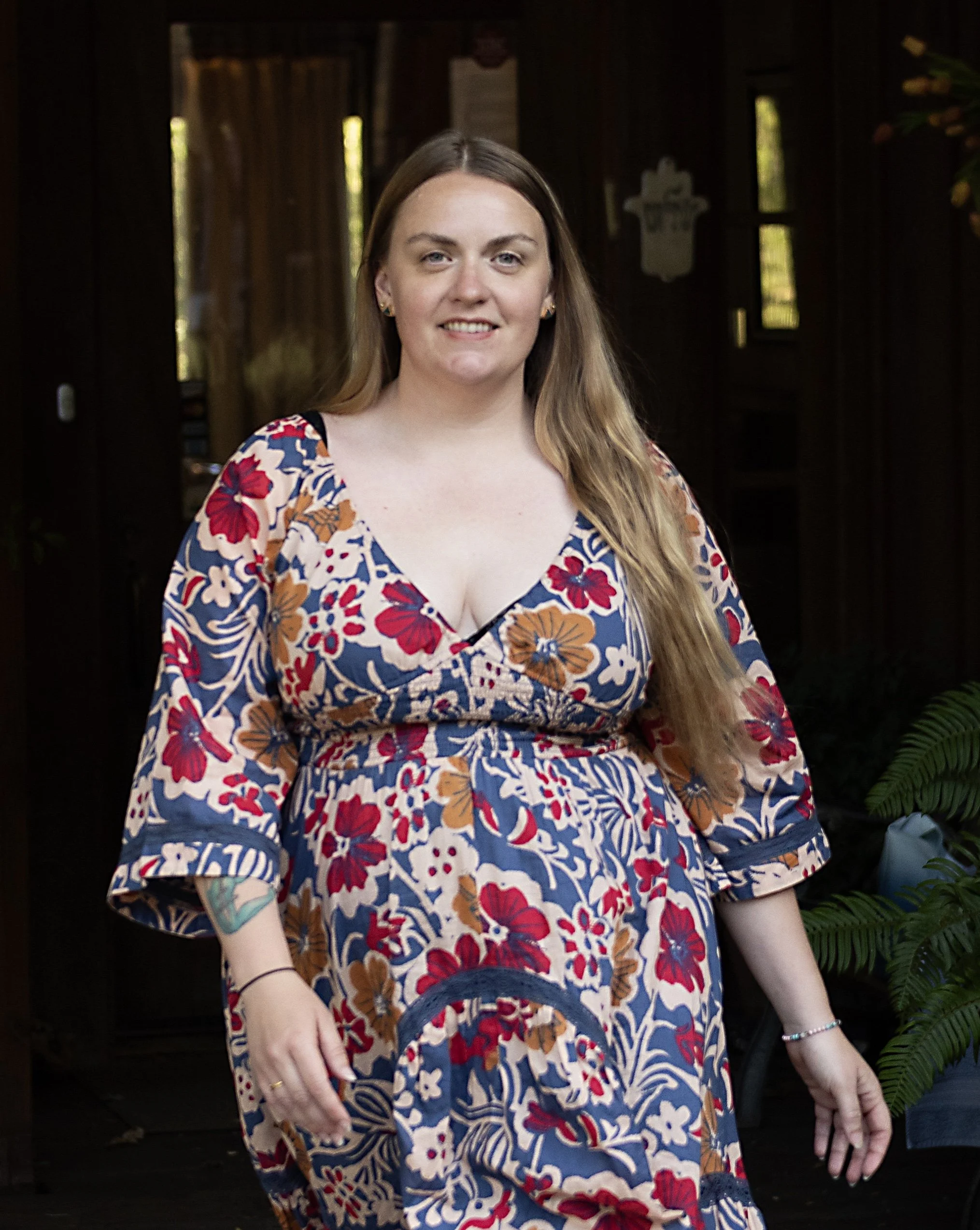 Portrait of a woman with long brown hair and a white sweater, smiling outdoors in a grassy field.