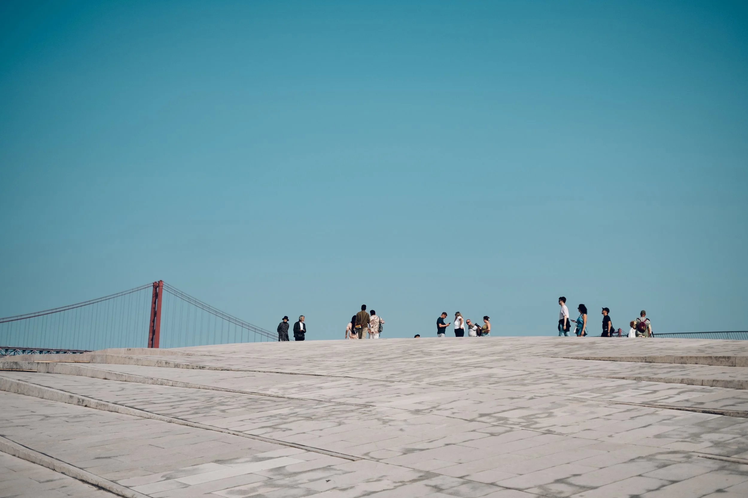 People walking and standing on a large open paved area near the Golden Gate Bridge on a clear day