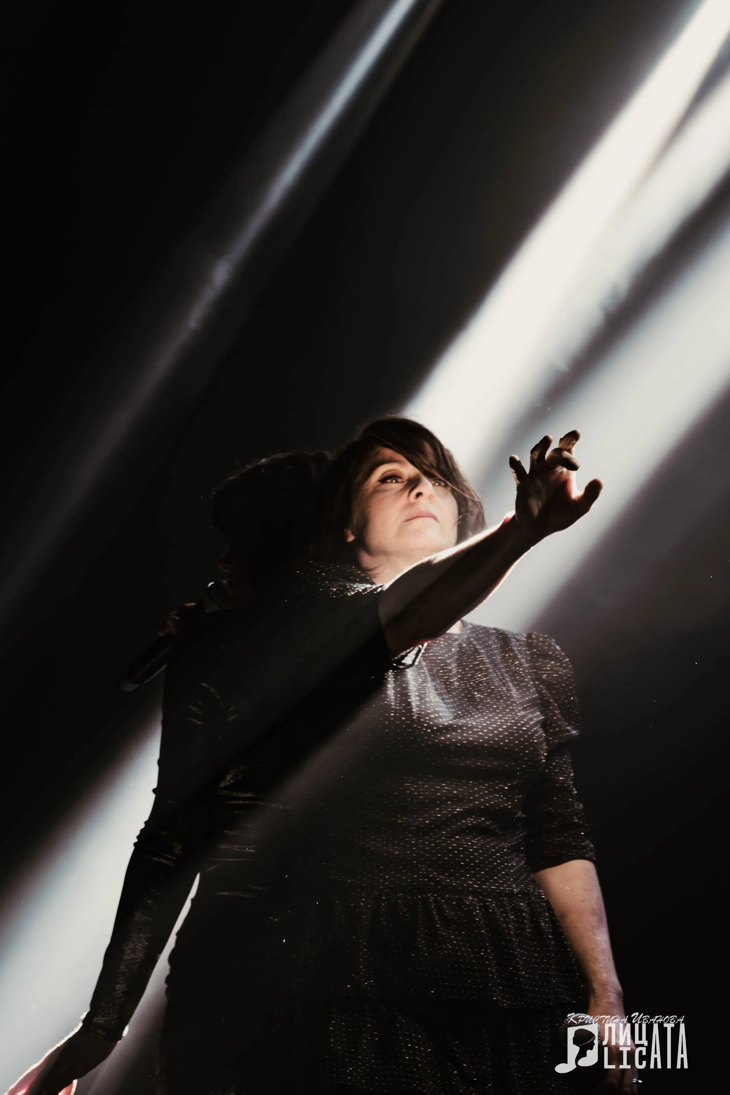 Nouvelle Vague French band on stage. A female performer on stage, reaching upward with her hand, holding a microphone in her other hand, with dramatic lighting highlighting her face and body.