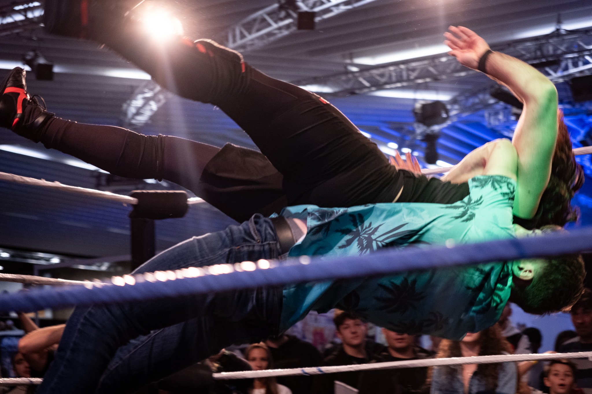 Two wrestlers on the mat during a wrestling match, with an audience watching in the background. One wrestler is applying a headlock to the other.