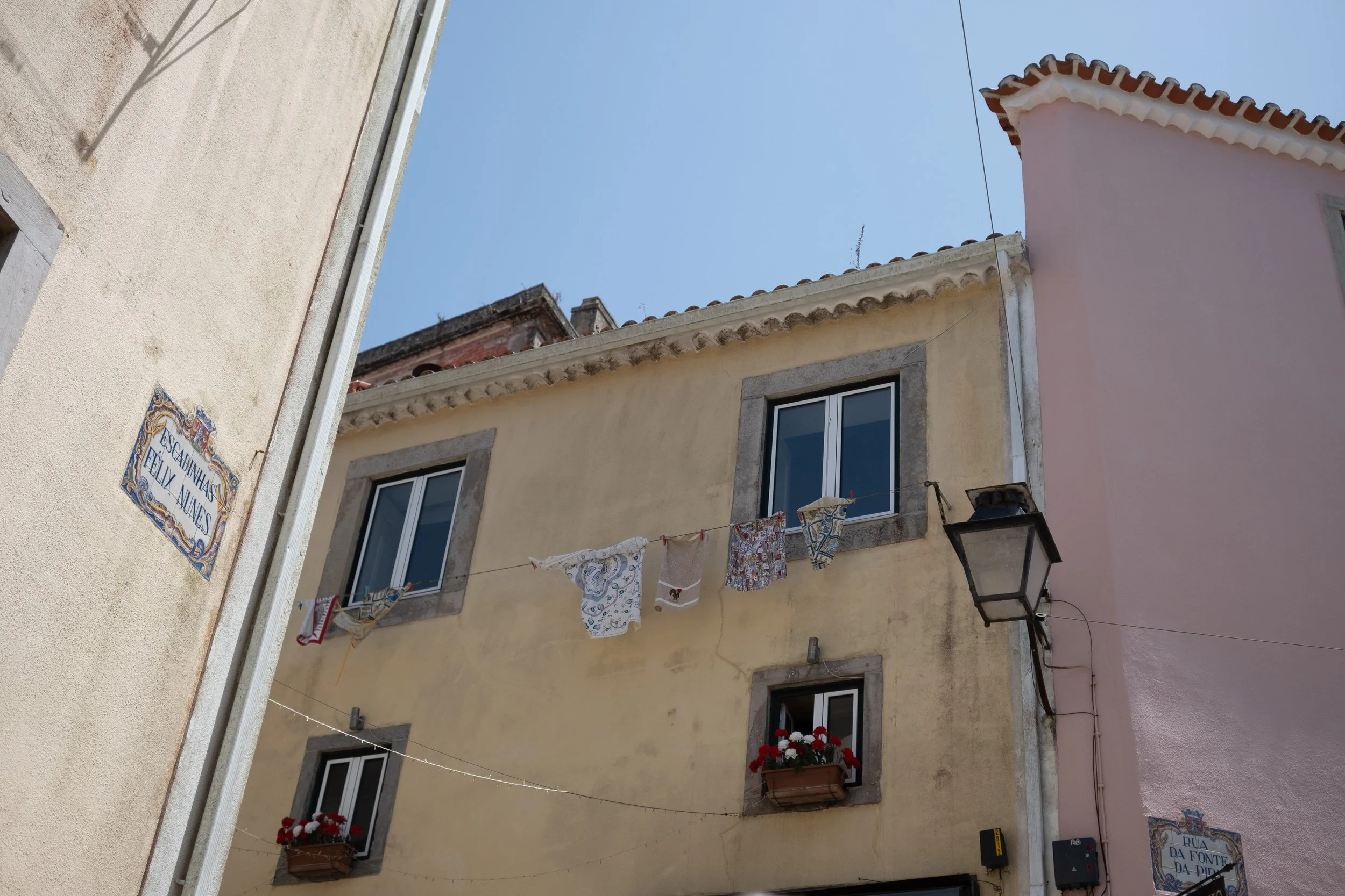 Colorful buildings with laundry hanging on a line, flower pots on windows, street signs, and a bright blue sky.