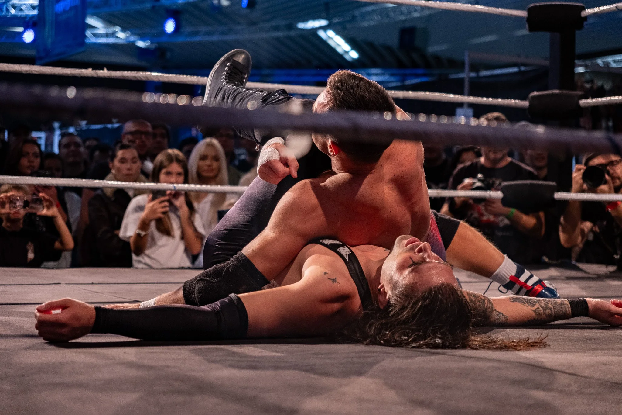 Two wrestlers engaged in a match inside a wrestling ring, with a crowd watching in the background.